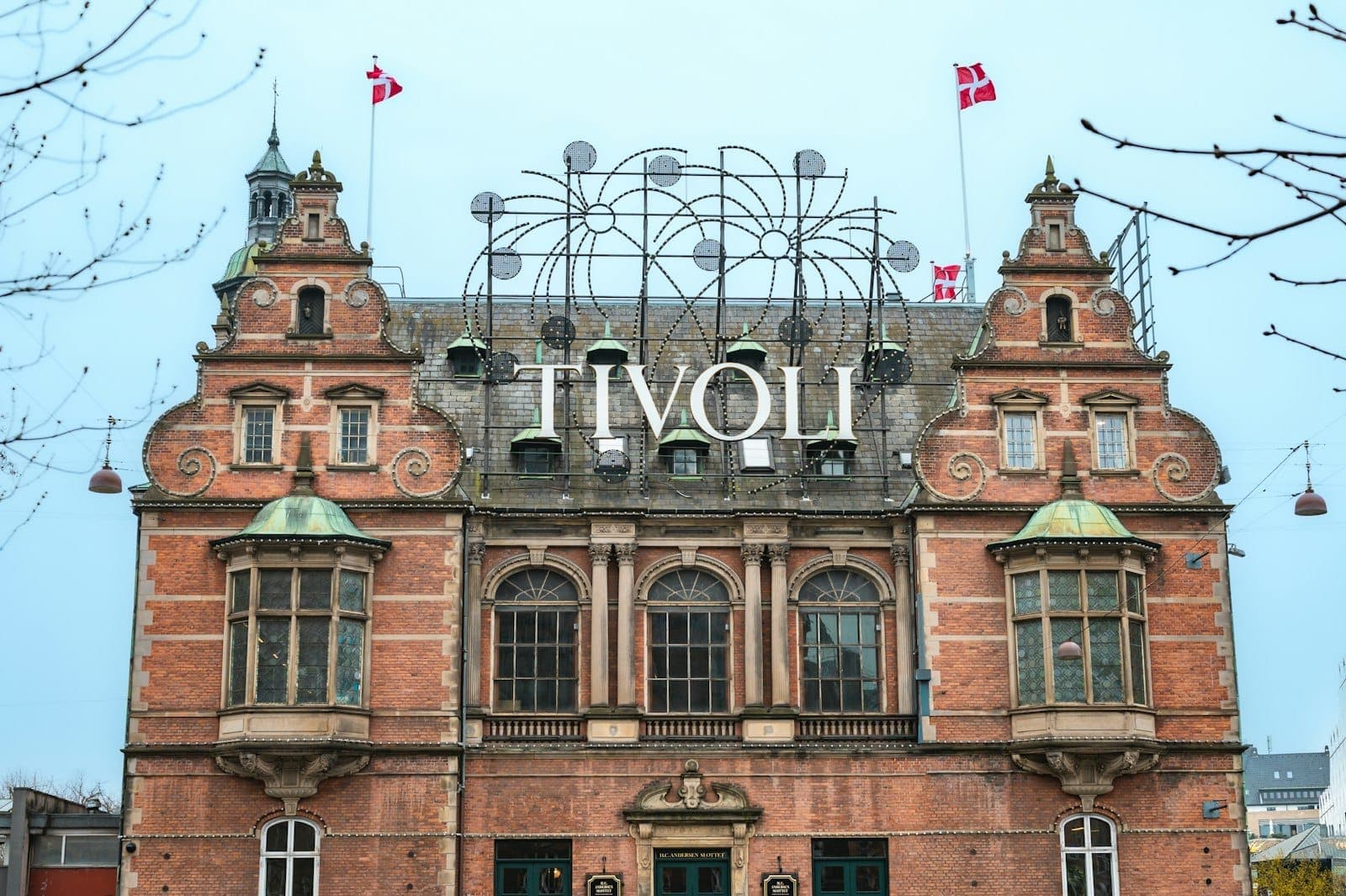 Frontowa fasada głównego wejścia do Tivoli Gardens w Kopenhadze z duńskimi flagami i ikonicznym szyldem, sfotografowana w świetle dziennym z wyraźnym widokiem na architekturę.