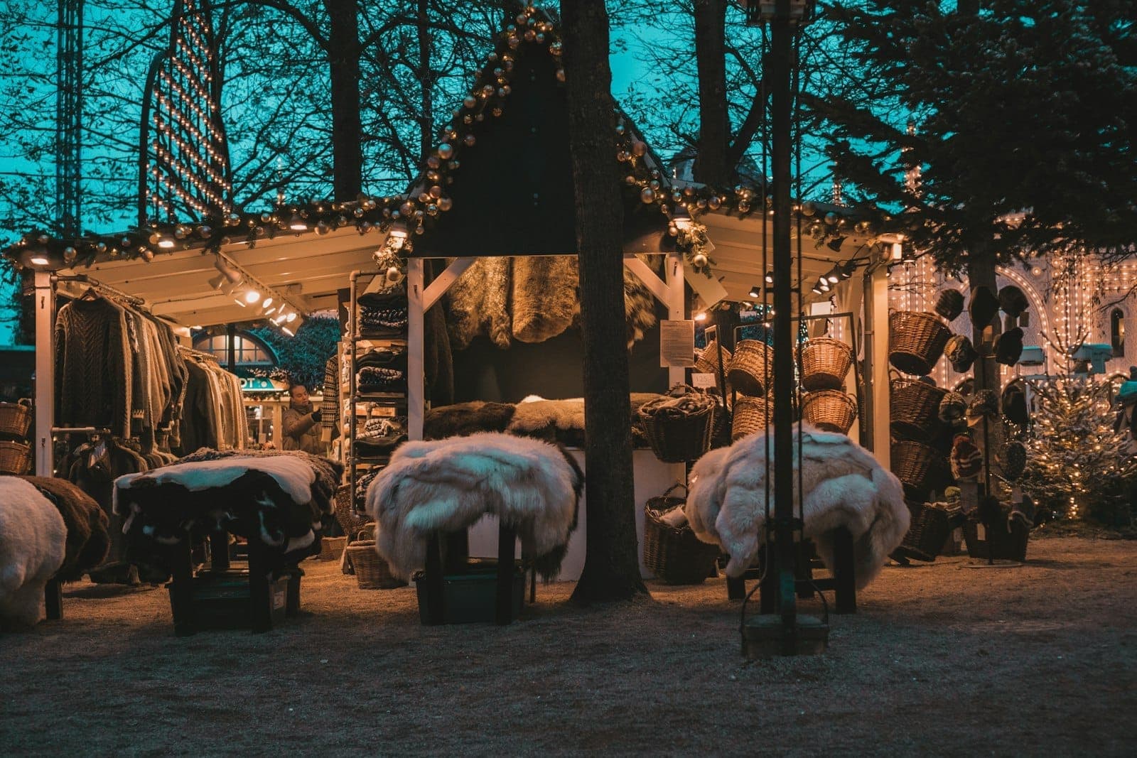 Ein gemütlicher Weihnachtsmarktstand in Kopenhagen, geschmückt mit Lichtern und mit Pelzen, Körben und festlichen Waren unter dem Abendhimmel.