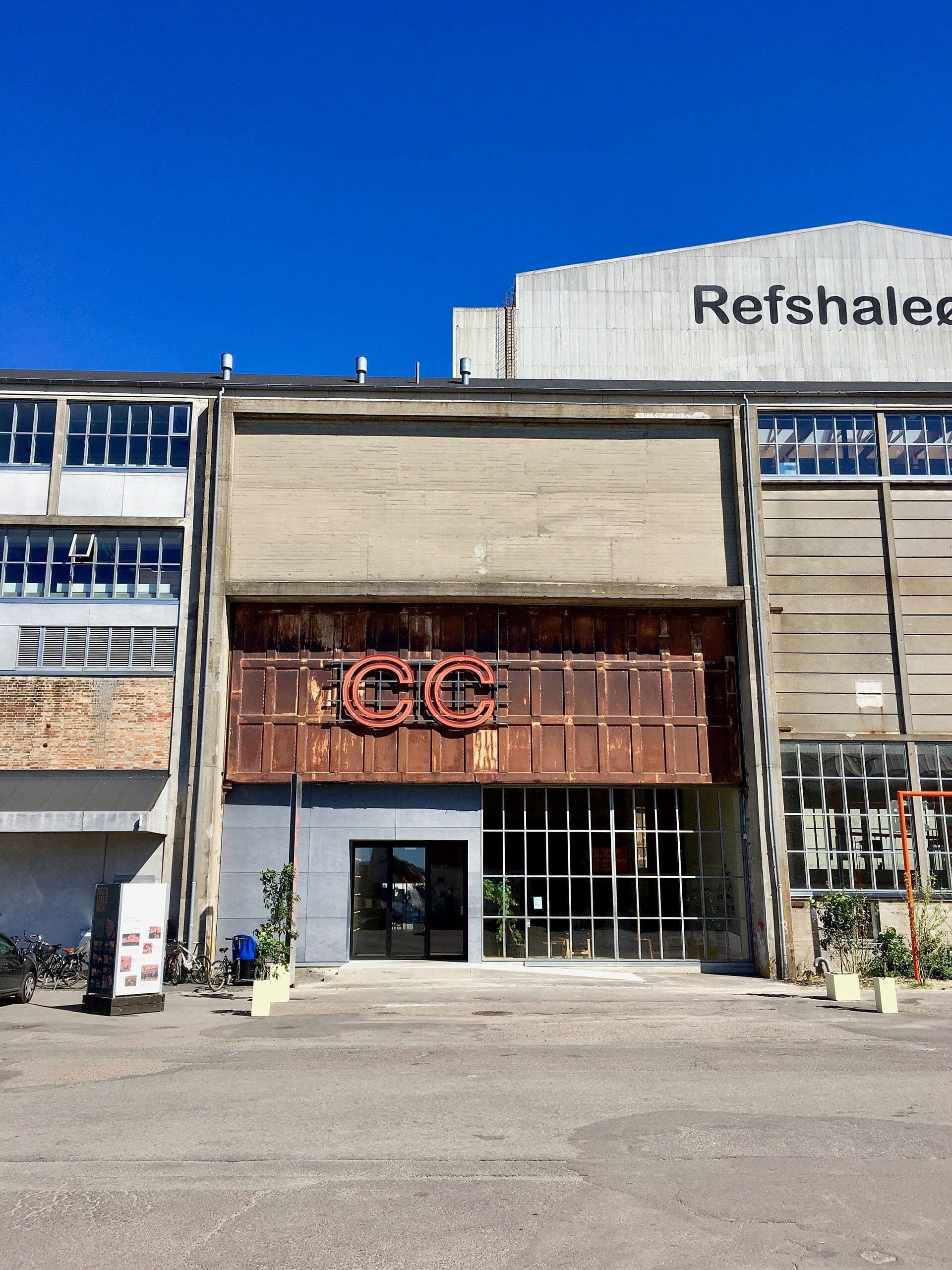 Vorderansicht des Copenhagen Contemporary-Gebäudes auf Refshaleøen mit industrieller Beton- und Metallfassade unter einem klaren blauen Himmel.