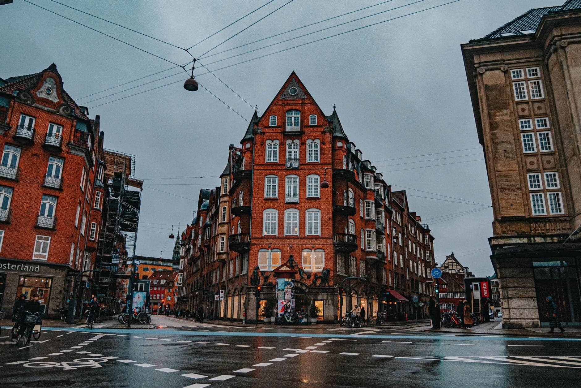 Una escena lluviosa en una calle del centro de Copenhague con edificios clásicos de ladrillo rojo, cielos nublados y pavimento mojado, capturando el clima típico de octubre.