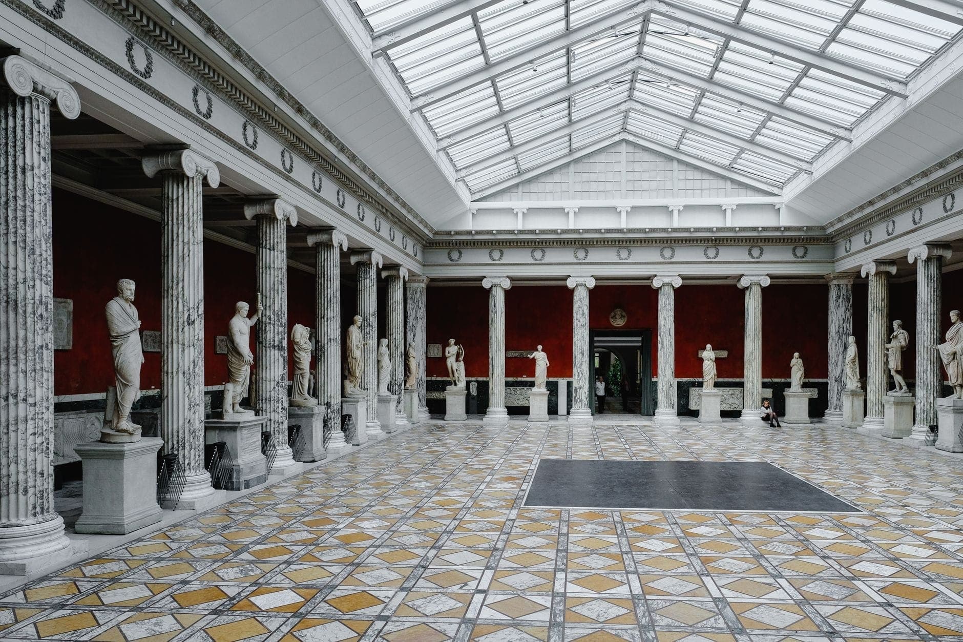 Vista amplia de un gran salón de museo en Copenhague con columnas de mármol, estatuas clásicas, techo con claraboya y suelo de colores con patrones.