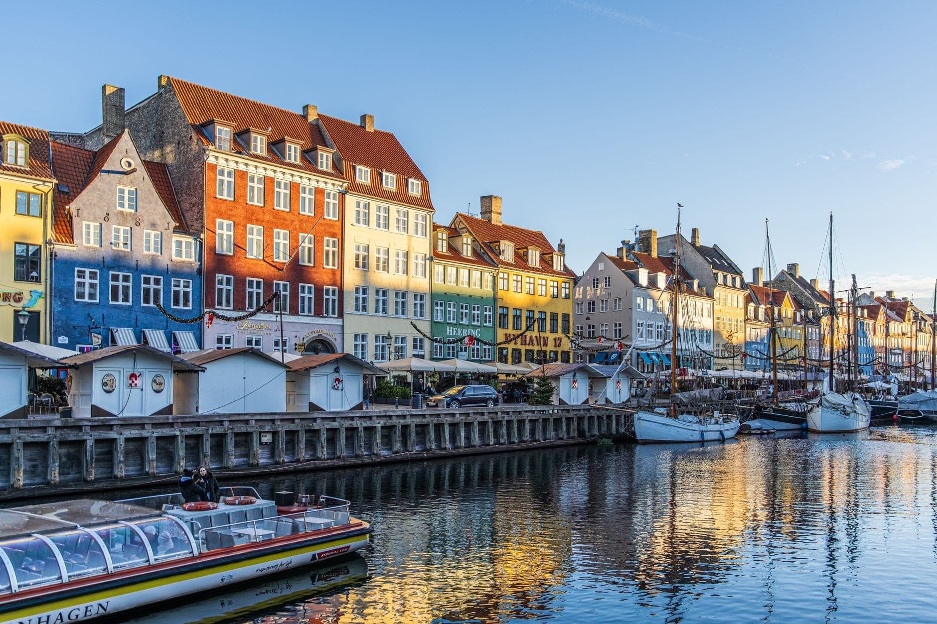 La lumière vive du soleil d'été illumine les maisons historiques colorées et les bateaux de Nyhavn à Copenhague, sous un ciel bleu dégagé avec des promeneurs profitant du front de mer.