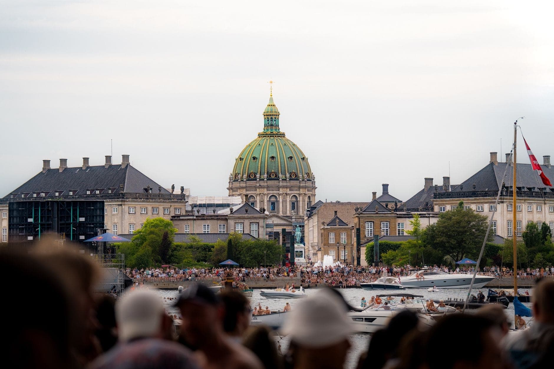 Grande foule estivale au bord de l'eau à Copenhague avec des bateaux et le dôme de la Marble Church visibles en arrière-plan.