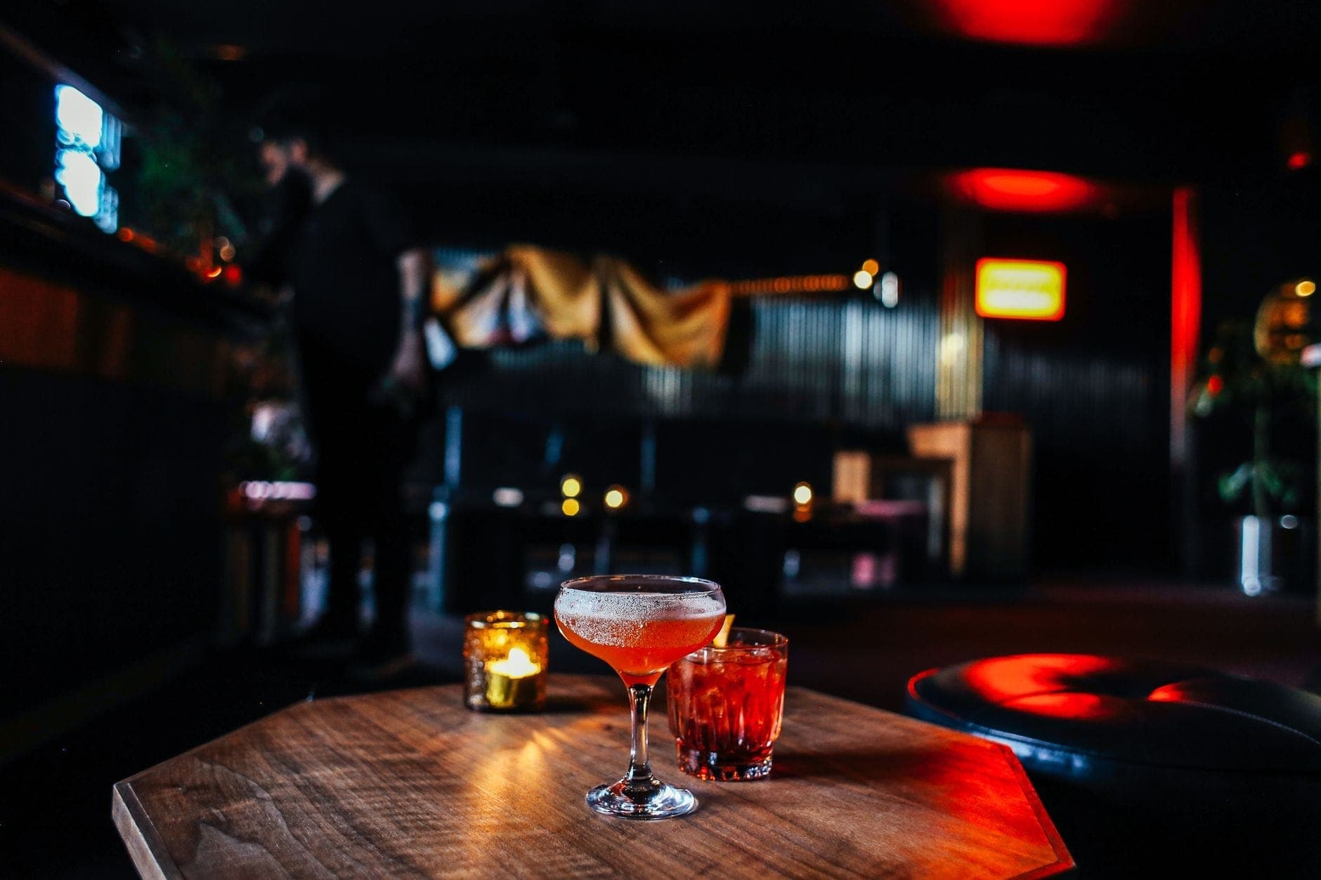 Interior de um bar em Copenhague com pouca luz, coquetéis sobre uma mesa, assentos aconchegantes e iluminação ambiente quente.