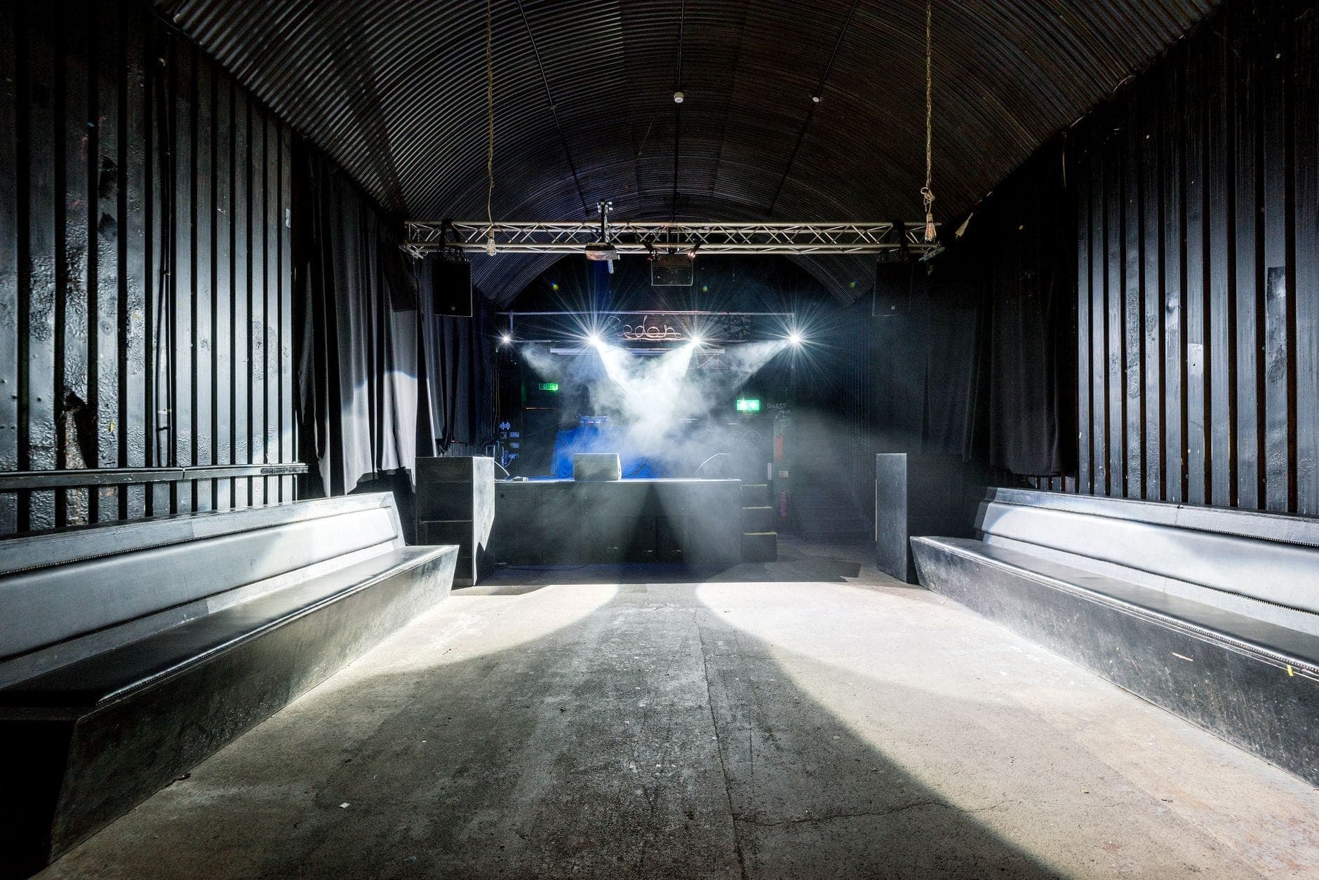 Interior vazio de uma discoteca com bancos, palco, cabine de DJ, iluminação dramática e decoração industrial preta, pronta para uma festa noturna em Copenhague.