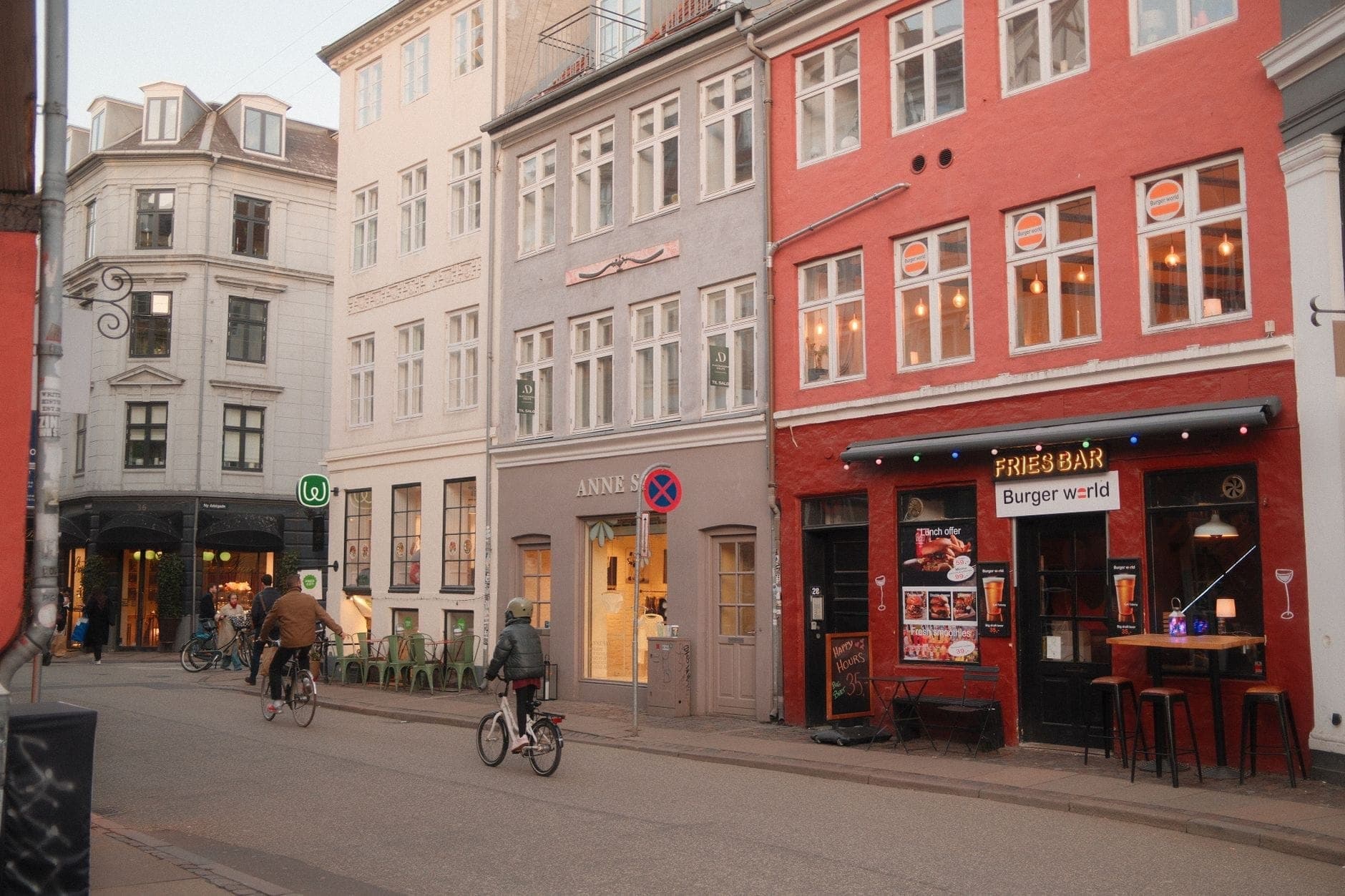 Calle en Copenhague con edificios coloridos, ciclistas y restaurantes económicos, que sugieren barrios locales asequibles.