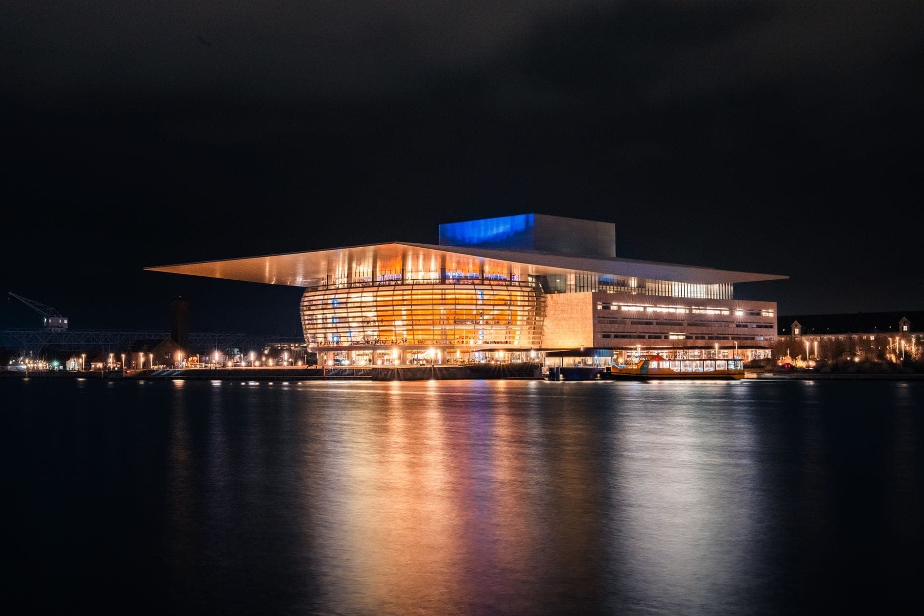 Das Kopenhagener Opernhaus bei Nacht, vom Hafen aus fotografiert – mit leuchtenden Spiegelungen auf dem Wasser und einer eindrucksvollen modernen Architektur.