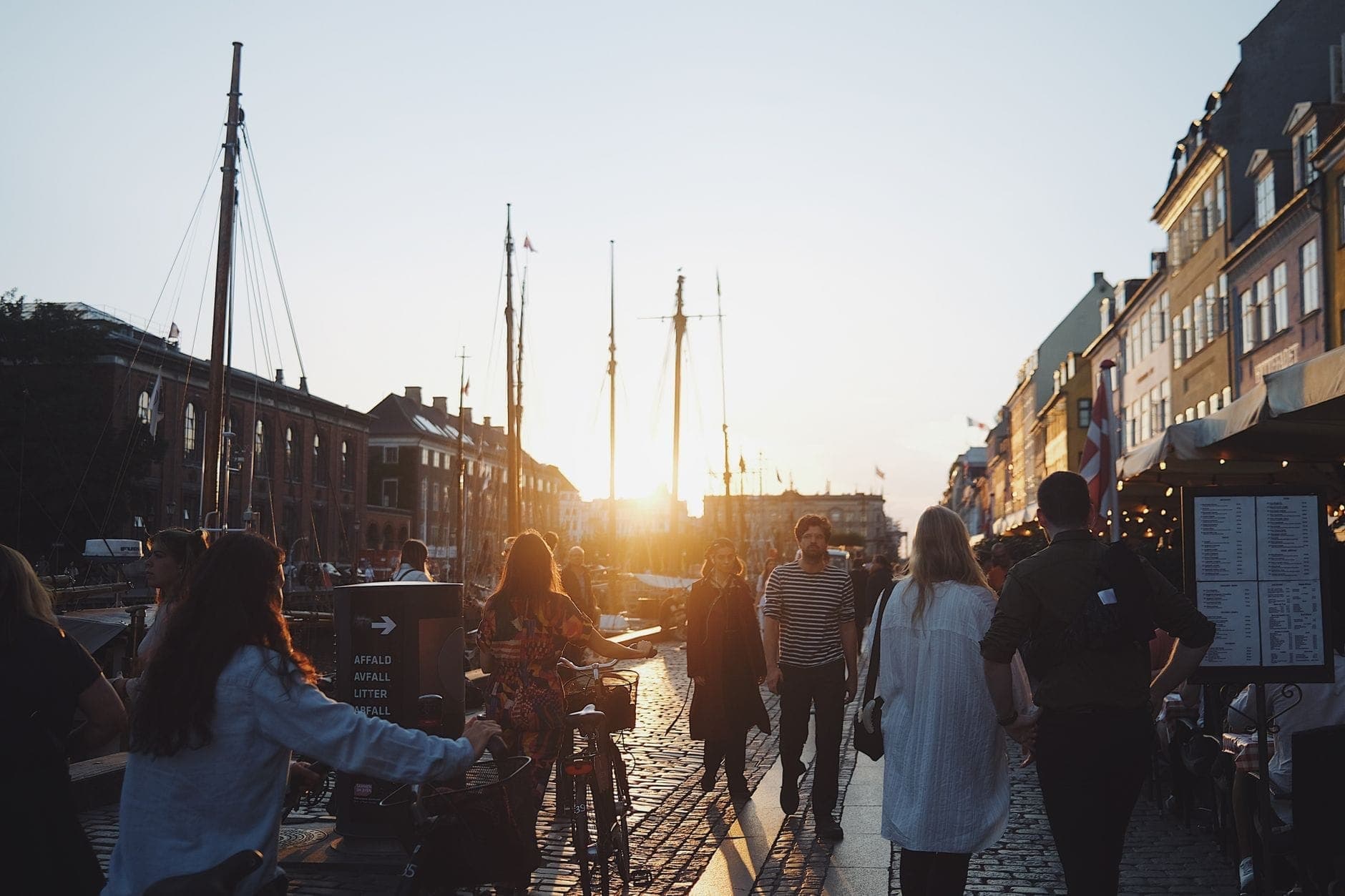 Mọi người đi dạo dọc kênh Nyhavn ở Copenhagen lúc hoàng hôn với những tòa nhà đầy màu sắc mang tính lịch sử và những chiếc thuyền xếp hàng dọc bờ kè.