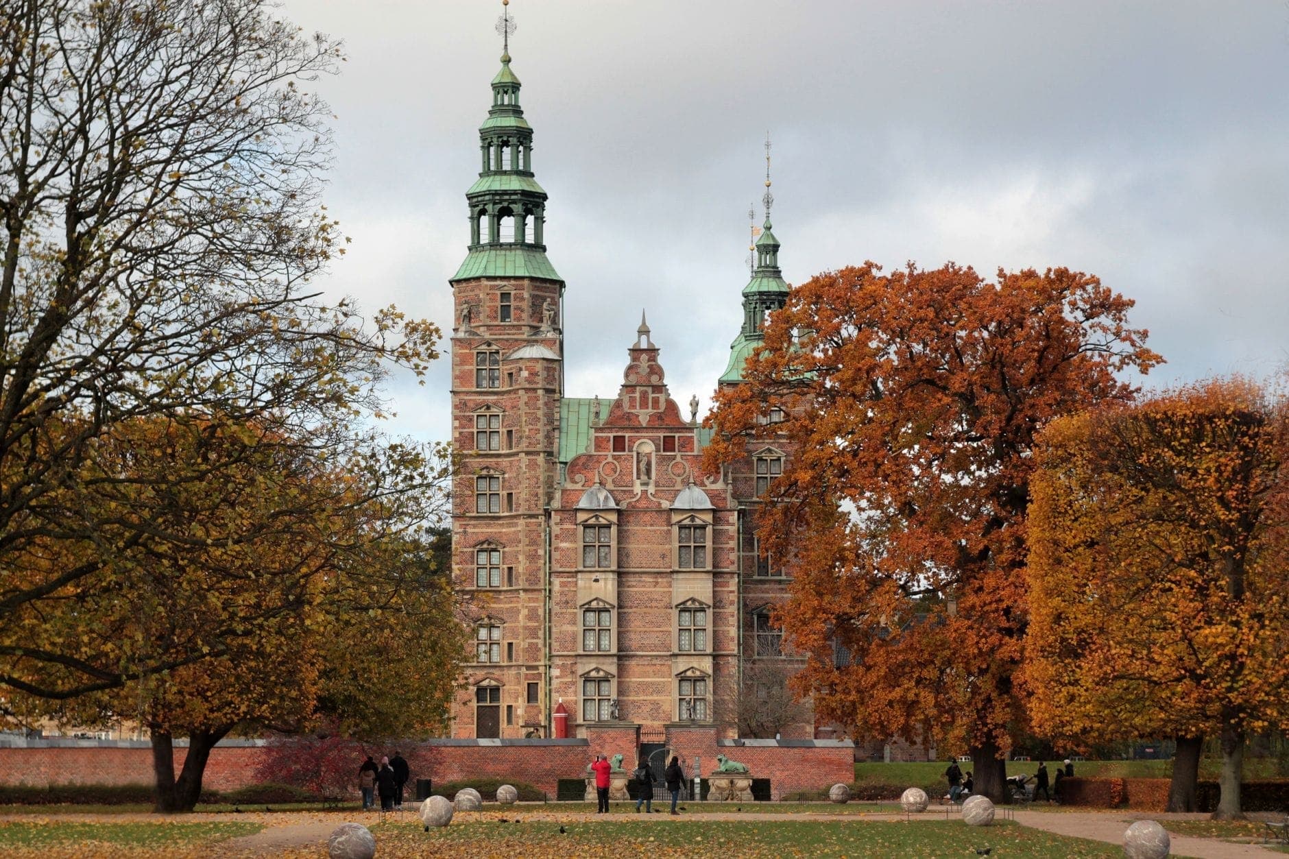 Blick auf Schloss Rosenborg in Kopenhagen mit Familien und Kindern, die im Park zwischen Herbstbäumen spazieren und spielen.