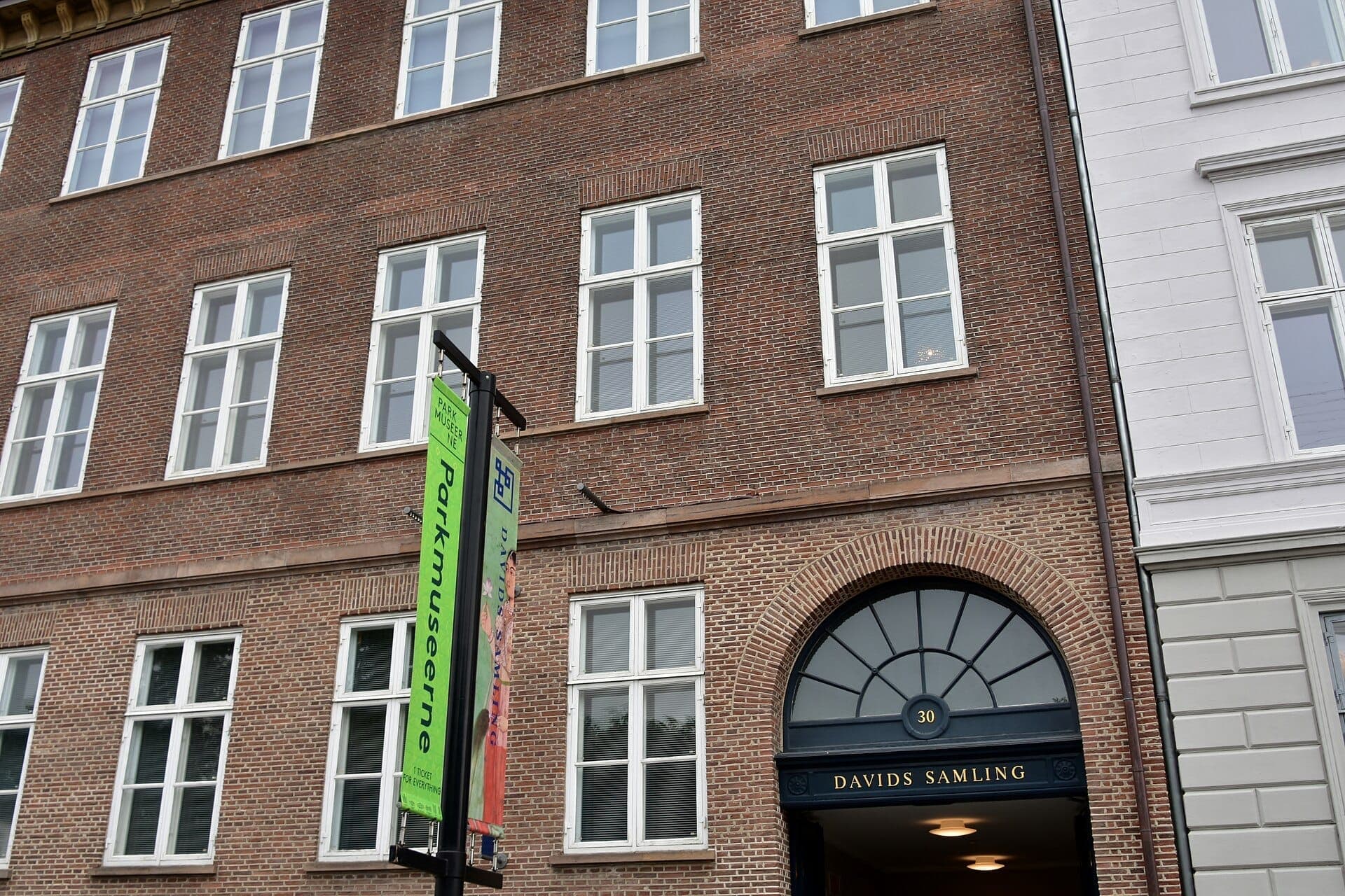 Fassade der David Collection in Kopenhagen mit rotem Backsteinäußeren, gewölbtem Eingang und Bannern für Parkmuseerne an einem bewölkten Tag.