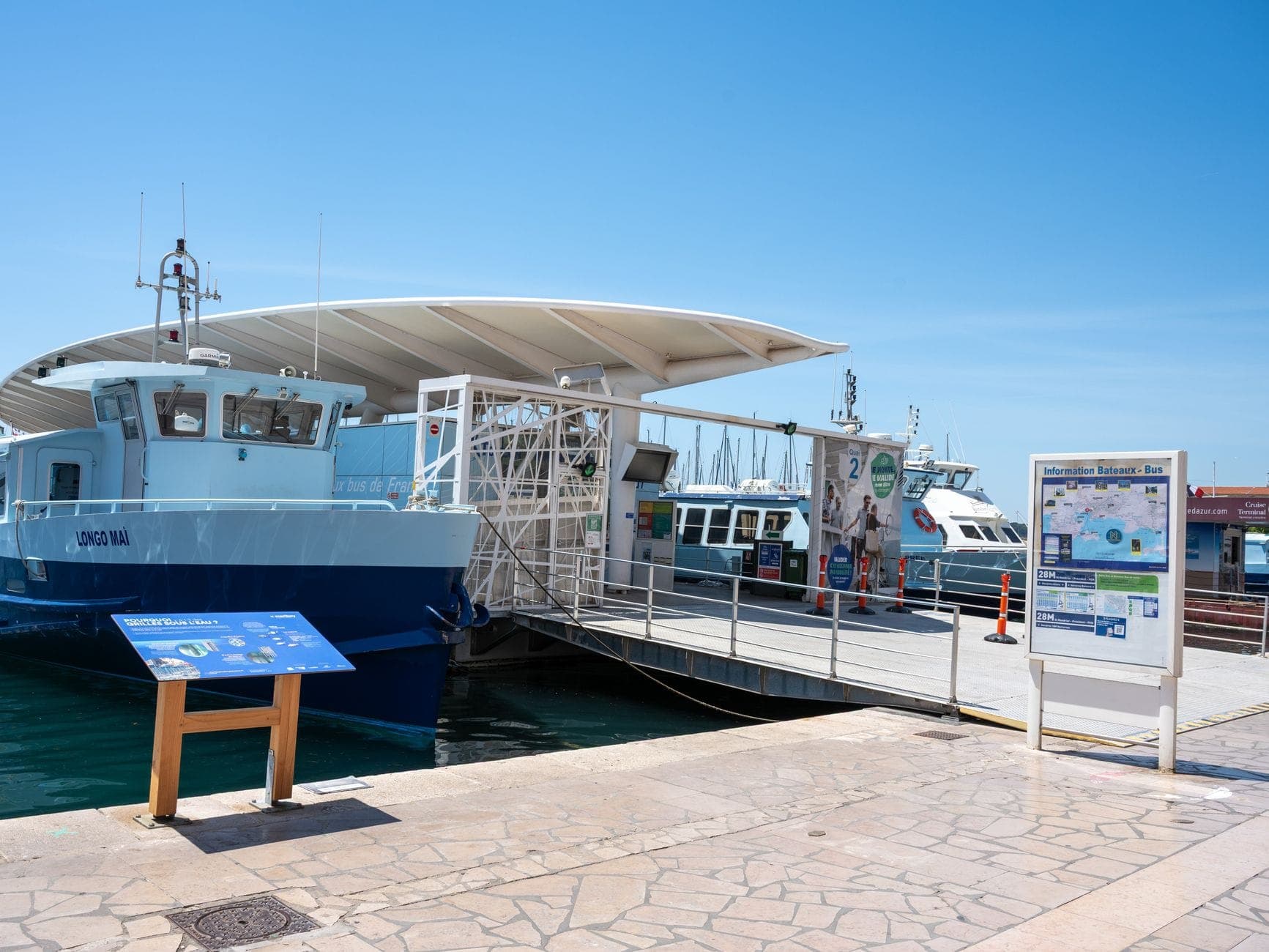Modern ferry terminal in Ibiza with docked passenger ferries, informational signs, and clear blue sky.