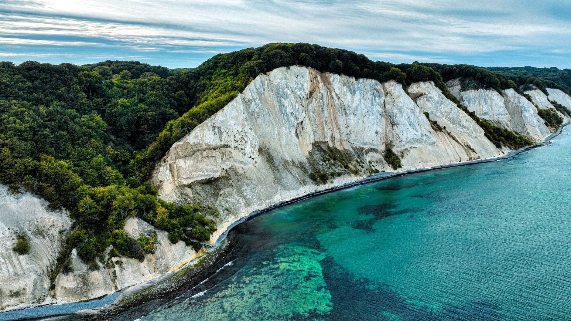 Drammatiche scogliere bianche di gesso si innalzano sopra il mare turchese con una lussureggiante foresta verde in cima, viste da una prospettiva aerea.