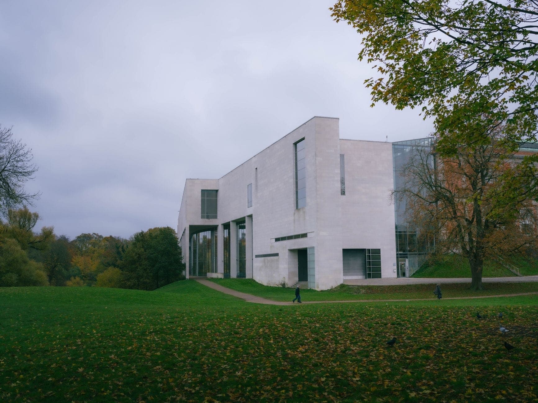 Un moderno edificio museale dai colori chiari si trova in un rigoglioso parco sotto un cielo nuvoloso, suggerendo una grande istituzione artistica nei pressi di Copenaghen.