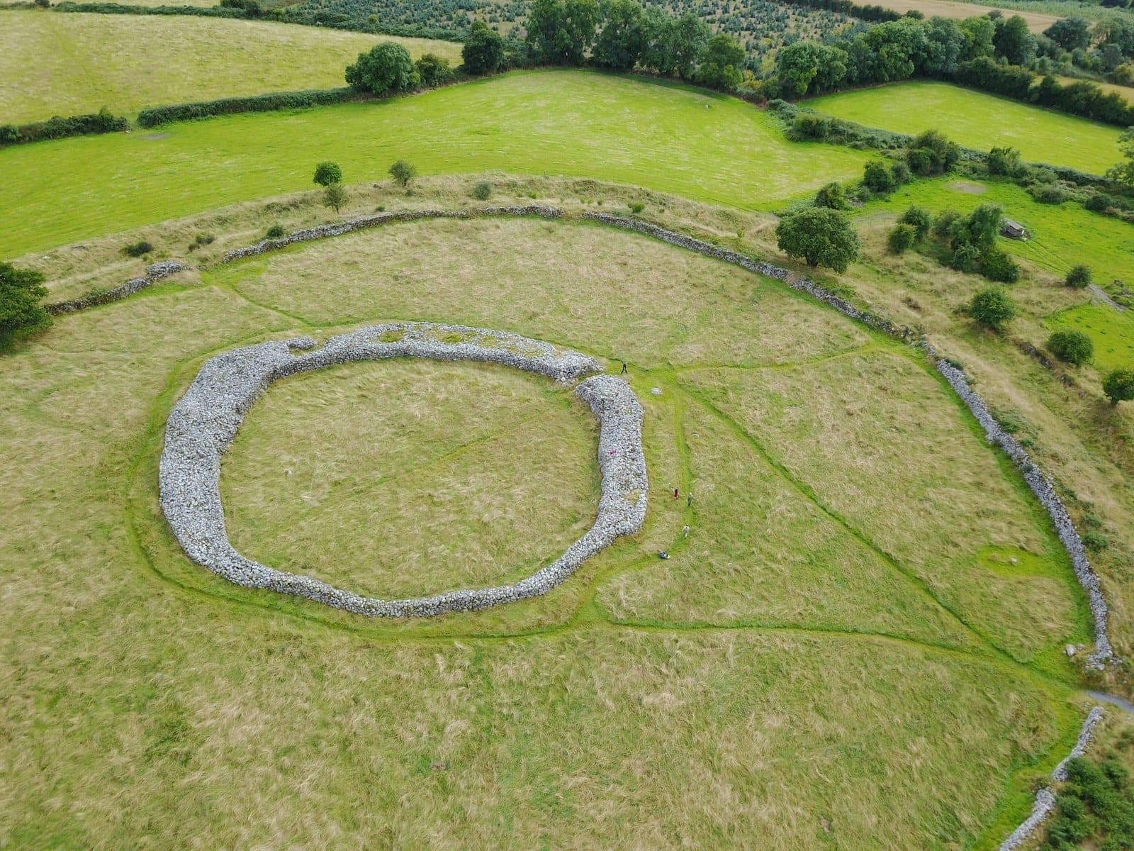 Vue aérienne d'un grand cercle de pierres préhistorique ou d'un fort circulaire dans un champ herbeux entouré d'une campagne vallonnée et verdoyante.