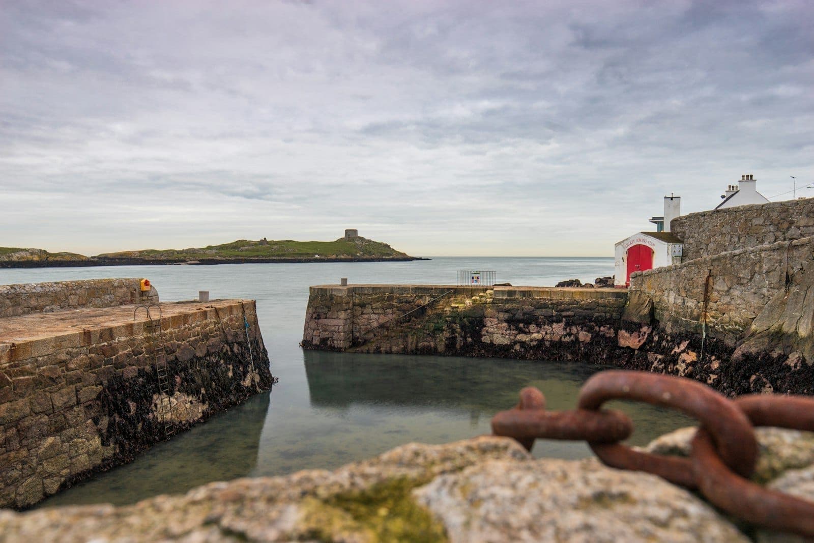 Petit port de pierre aux eaux calmes avec vue sur une île pittoresque et une tour Martello, typique des villages côtiers de Dublin.