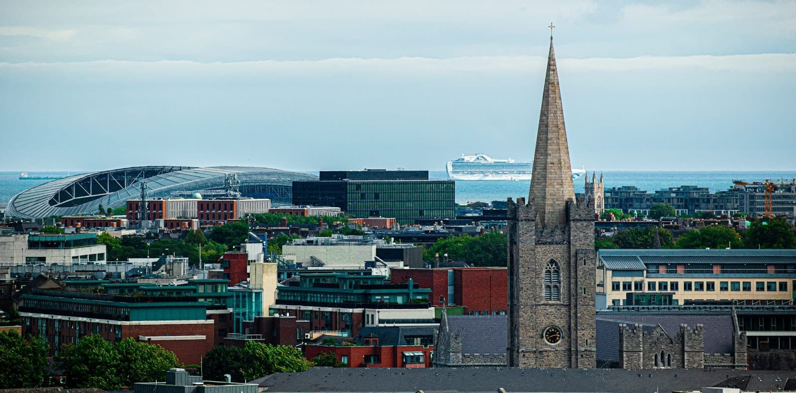 Vue panoramique de Dublin avec la flèche de la cathédrale St Patrick, l'Aviva Stadium et un ferry au loin sur la mer d'Irlande sous un ciel bleu.