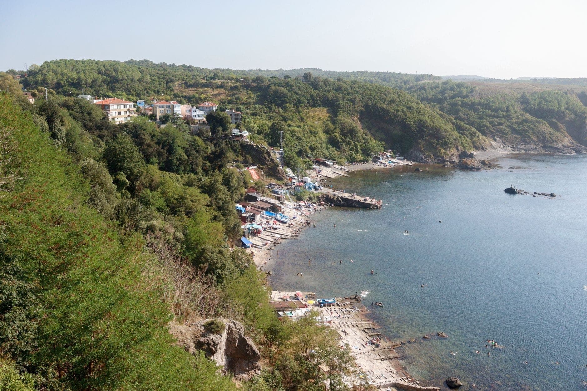 Widok z lotu ptaka na małą nadmorską wioskę z domami, piaszczystą plażą, skalistą linią brzegową i zielonymi wzgórzami na wybrzeżu Morza Czarnego niedaleko Stambułu.