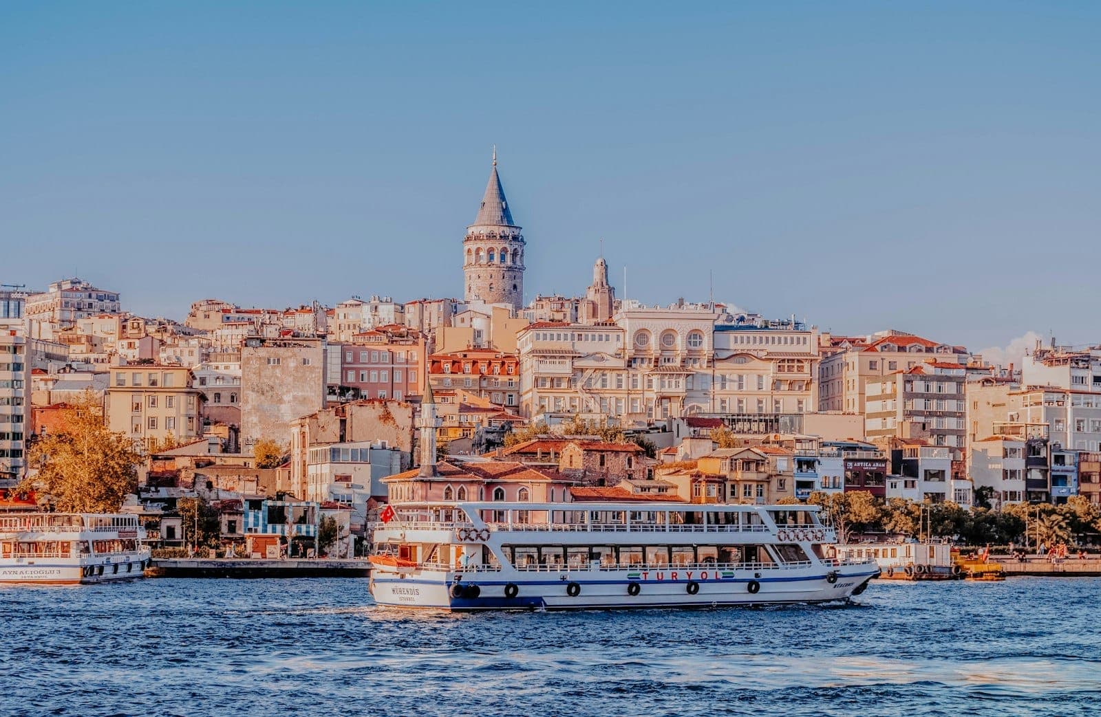 Panoramablick auf Istanbul mit dem Galata-Turm, historischen Gebäuden und Fähren auf dem Bosporus unter strahlend blauem Himmel.