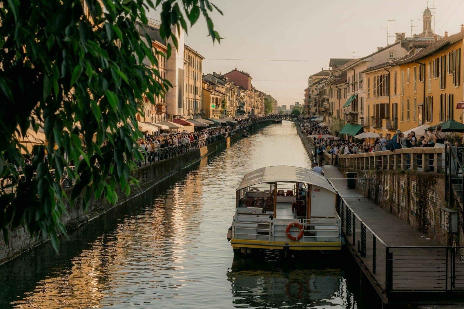 Canal scene at sunset with a boat, lively promenade, and rows of colorful buildings, capturing the charm of Milan’s easily accessible day trip destinations.