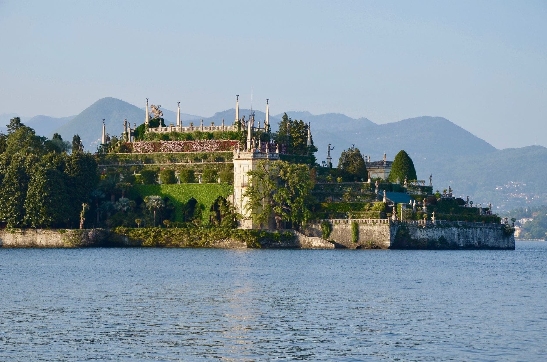 Vista nitida di Isola Bella sul Lago Maggiore, con il Palazzo Borromeo e i giardini barocchi terrazzati, con le montagne sullo sfondo.