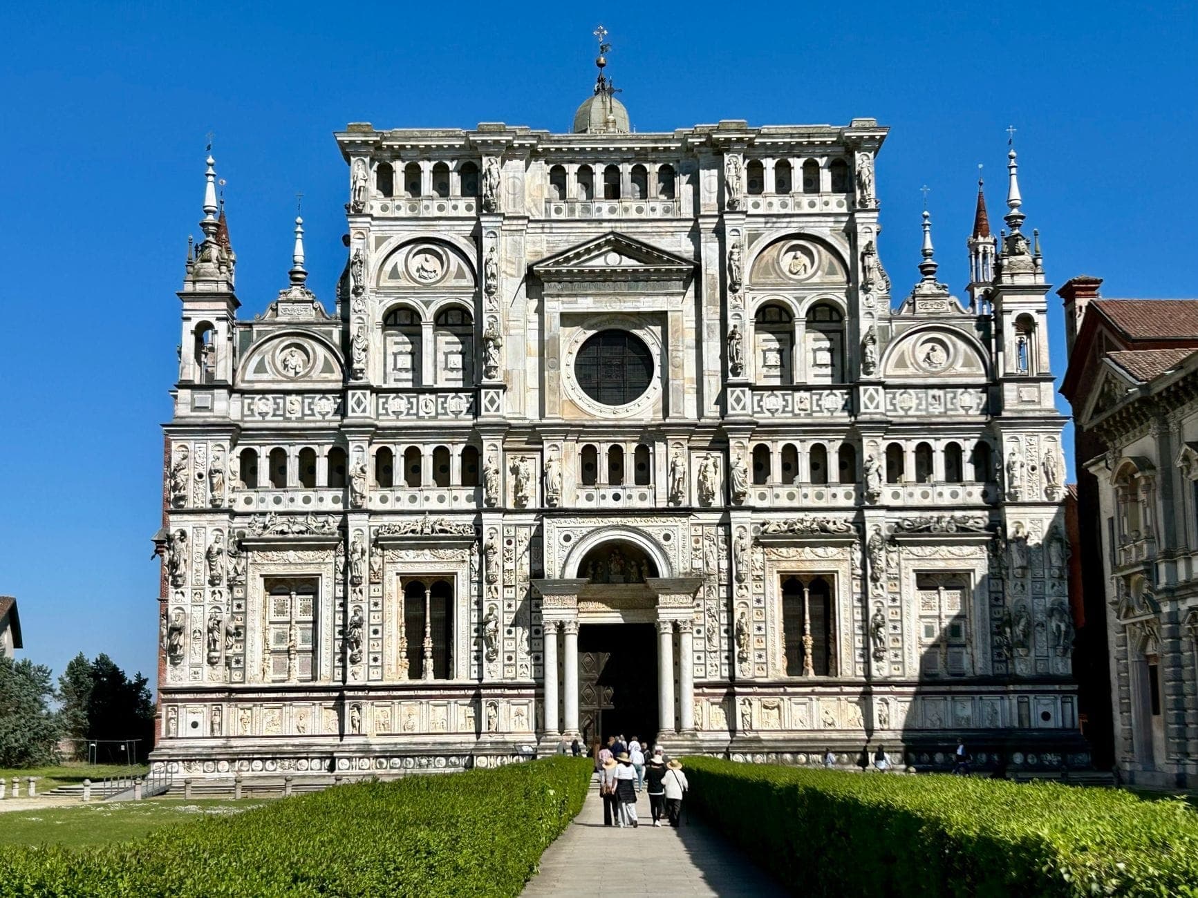 Facciata ornata in marmo bianco del monastero Certosa di Pavia con visitatori che camminano verso l'ingresso in una giornata di sole