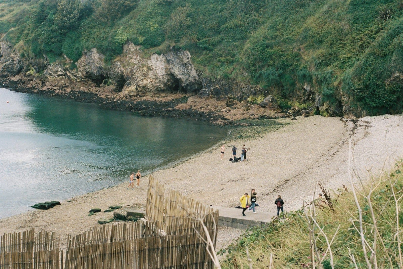 Ein kleiner, geschützter Sandstrand zwischen felsigen Klippen und Grün, auf dem Menschen spazieren gehen und die Küstenlandschaft bei Dublin genießen.