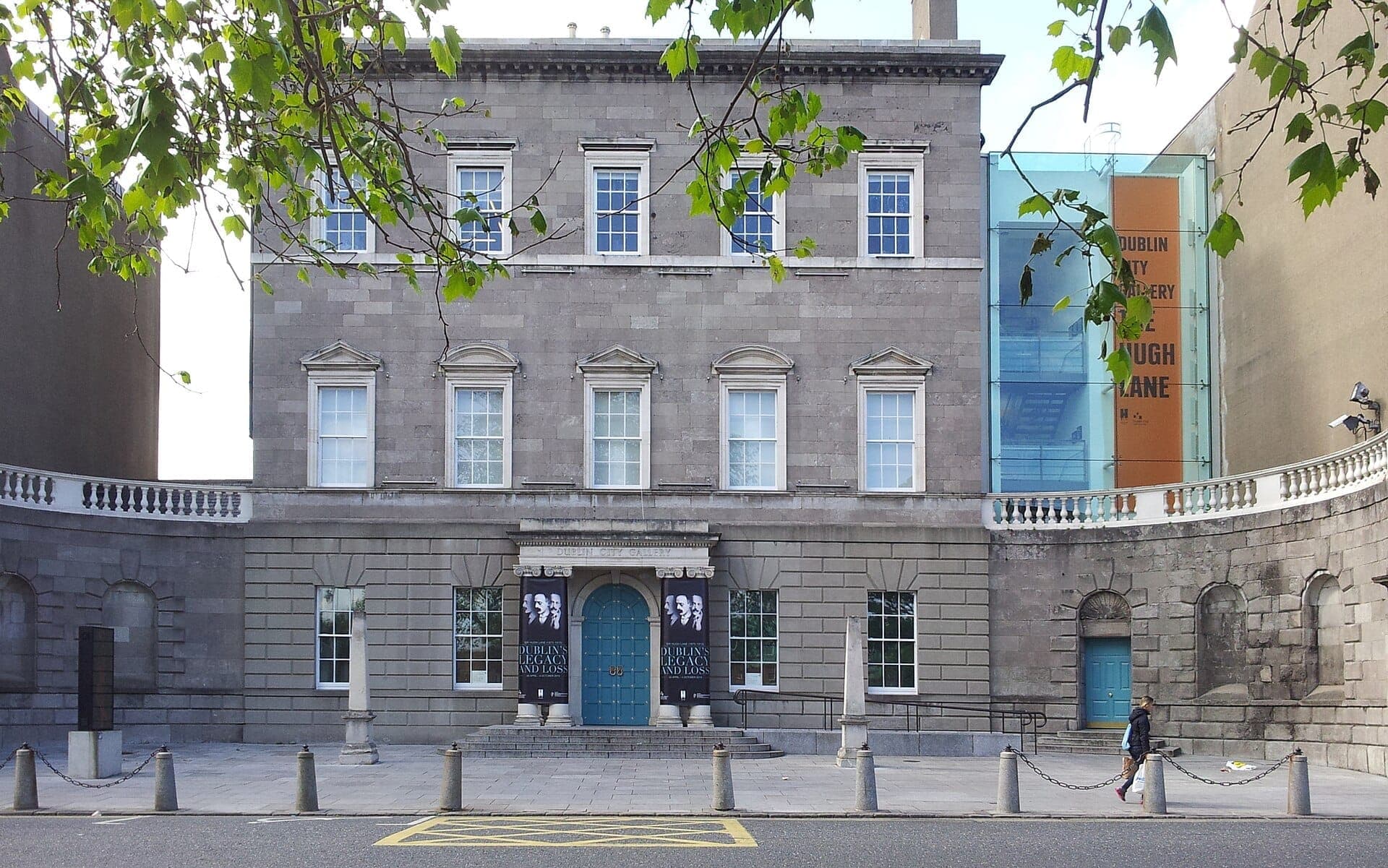 Vista frontal de la Dublin City Gallery The Hugh Lane, un majestuoso edificio georgiano con fachada de piedra, ventanas arqueadas y una puerta de entrada azul.