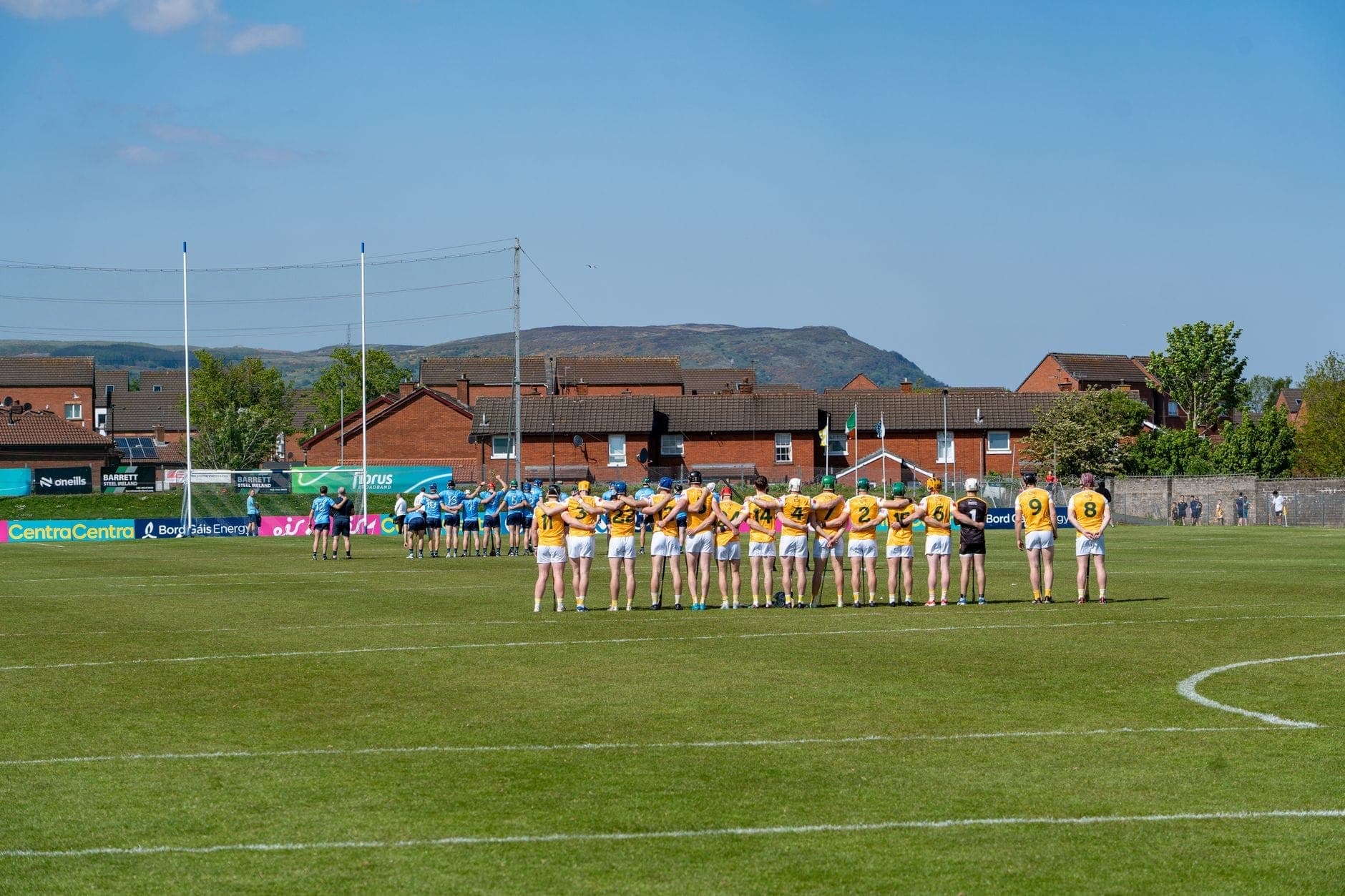 Gaelic-Football-Teams treten an einem sonnigen Spieltag auf einem grünen Rasen an, im Hintergrund Berge und Dubliner Häuser.