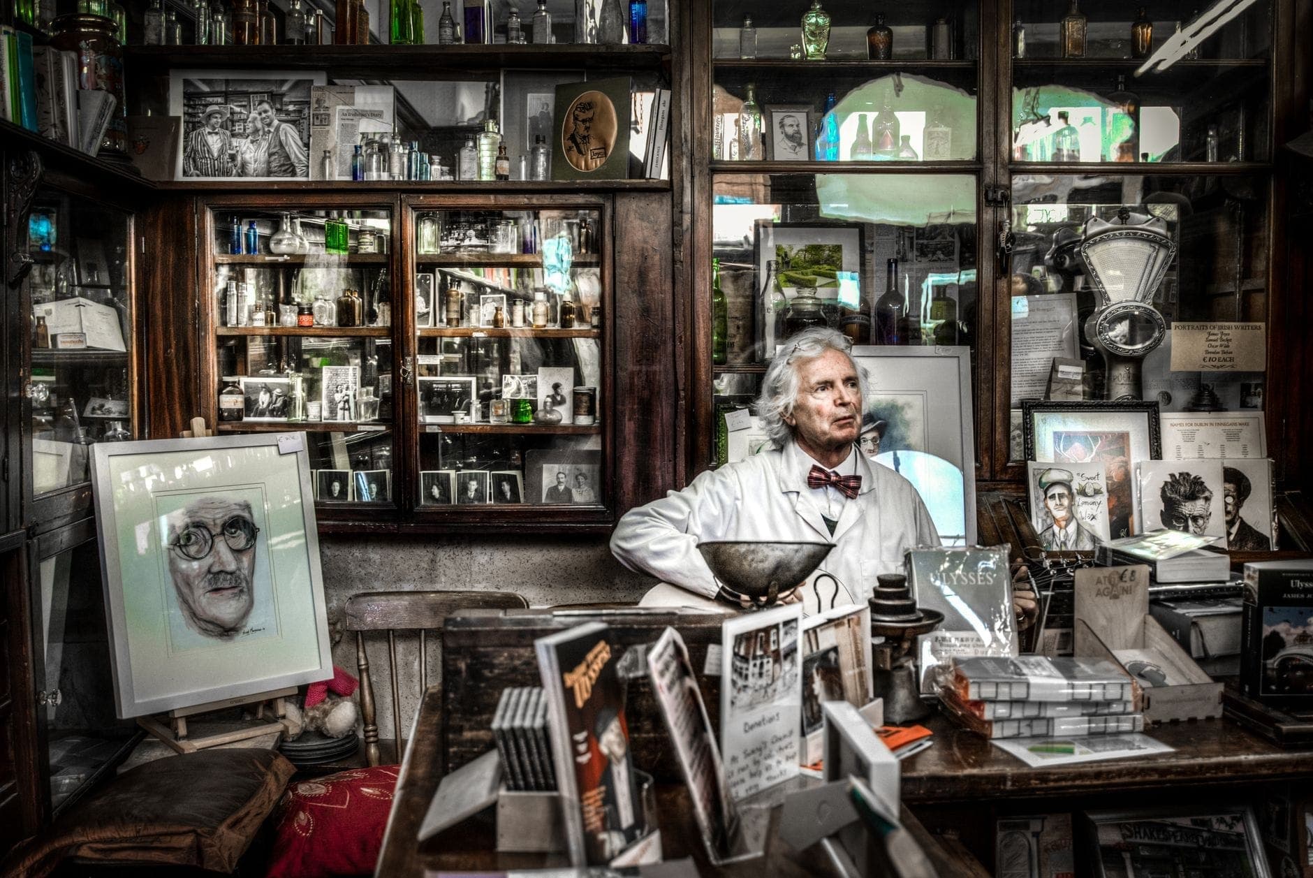Interno di un'antica farmacia o negozio a tema letterario a Dublino, con scaffali di bottiglie e libri, disegni di famosi scrittori e una persona in camice bianco.