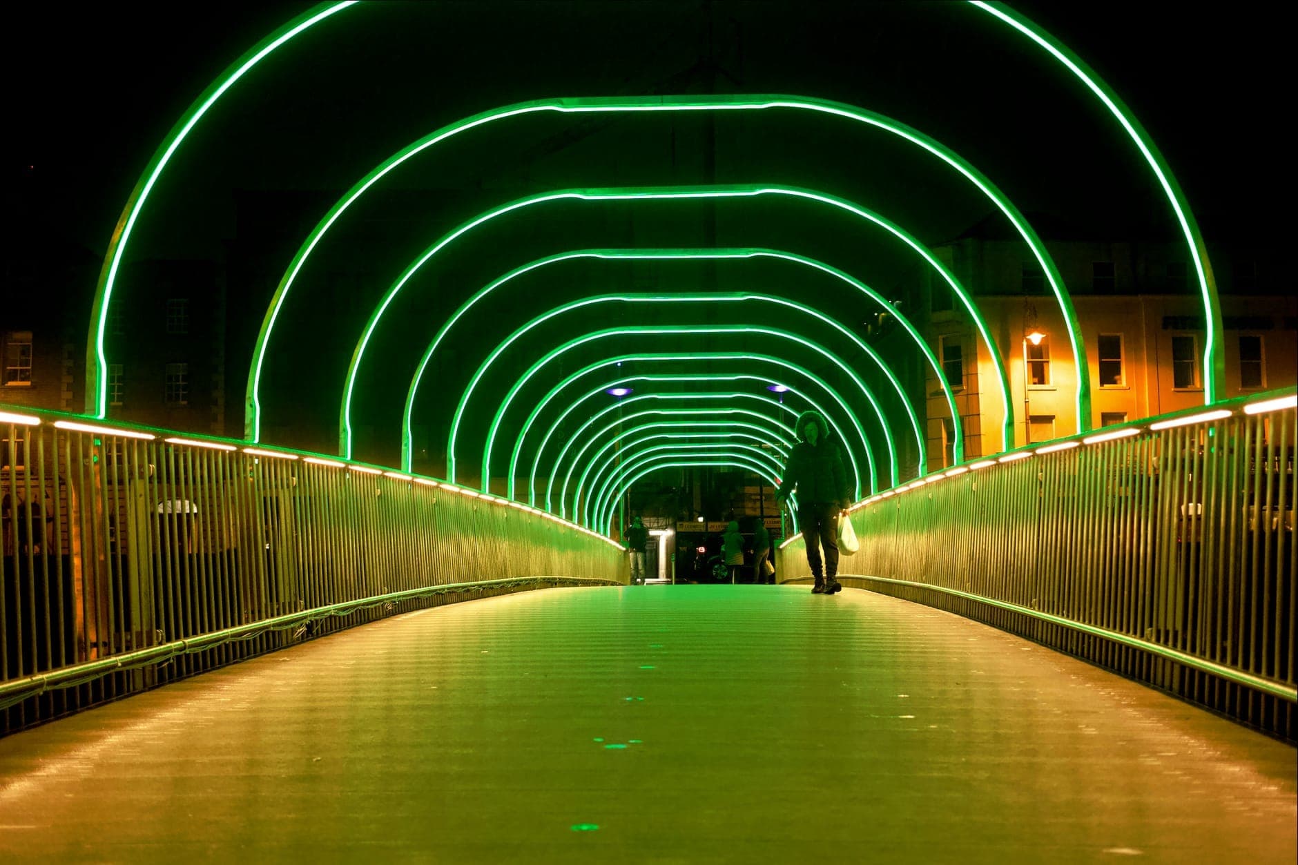 Person, die nachts durch den Brückentunnel im Dubliner Stadtzentrum läuft, der mit leuchtend grünen festlichen Lichtbögen beleuchtet ist.