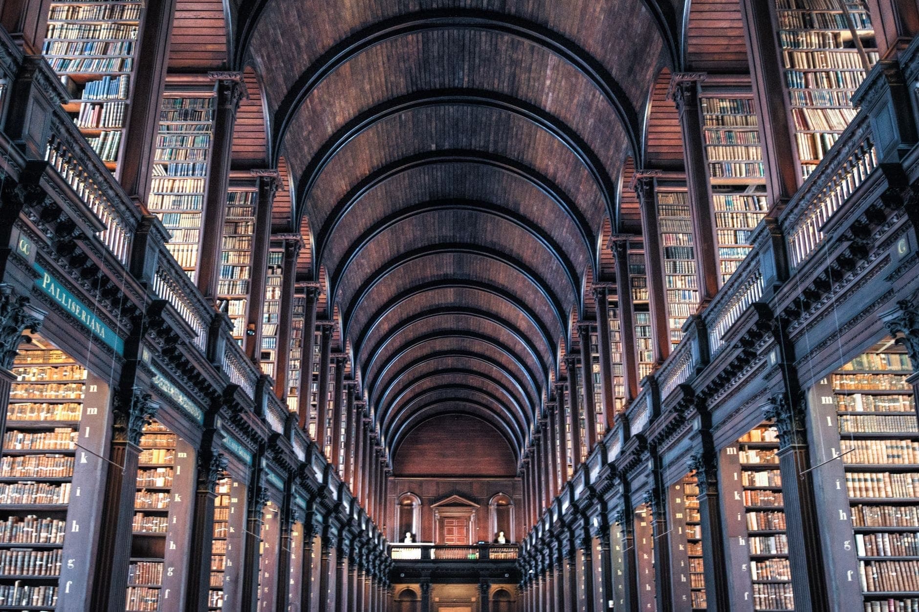 O teto abobadado de madeira e as enormes estantes da Long Room da Biblioteca do Trinity College em Dublin, repleta de livros e banhada em luz quente.