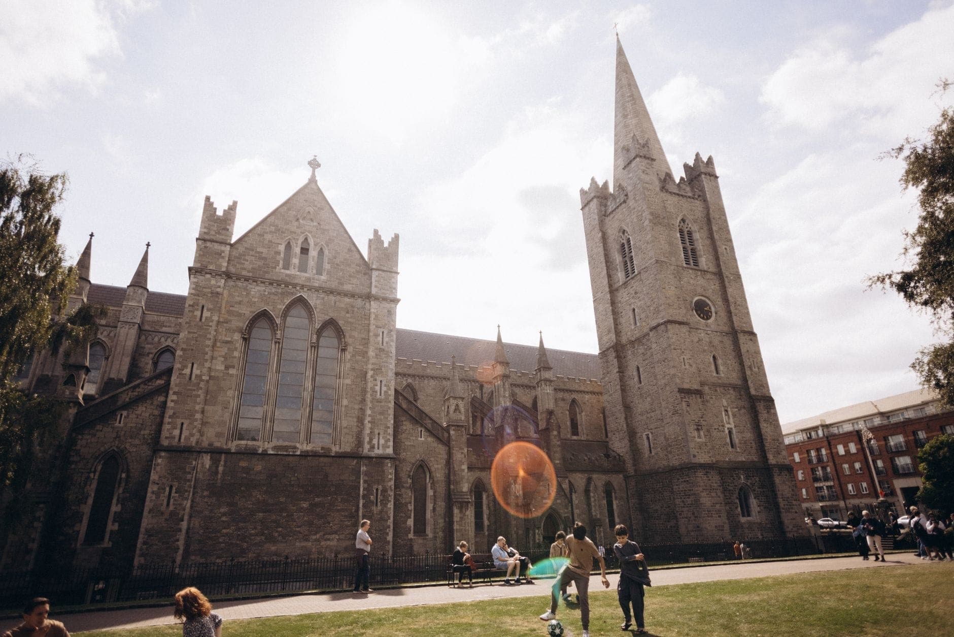 Vista grande angular da Catedral de St Patrick em Dublin com pessoas relaxando na grama em frente sob a luz do dia.