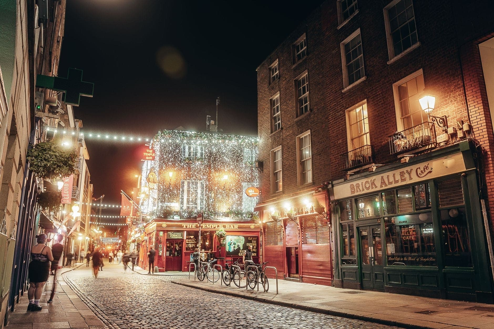 Strada acciottolata a Dublino di notte con pub animati, luci festose e persone che camminano nell'area di Temple Bar.