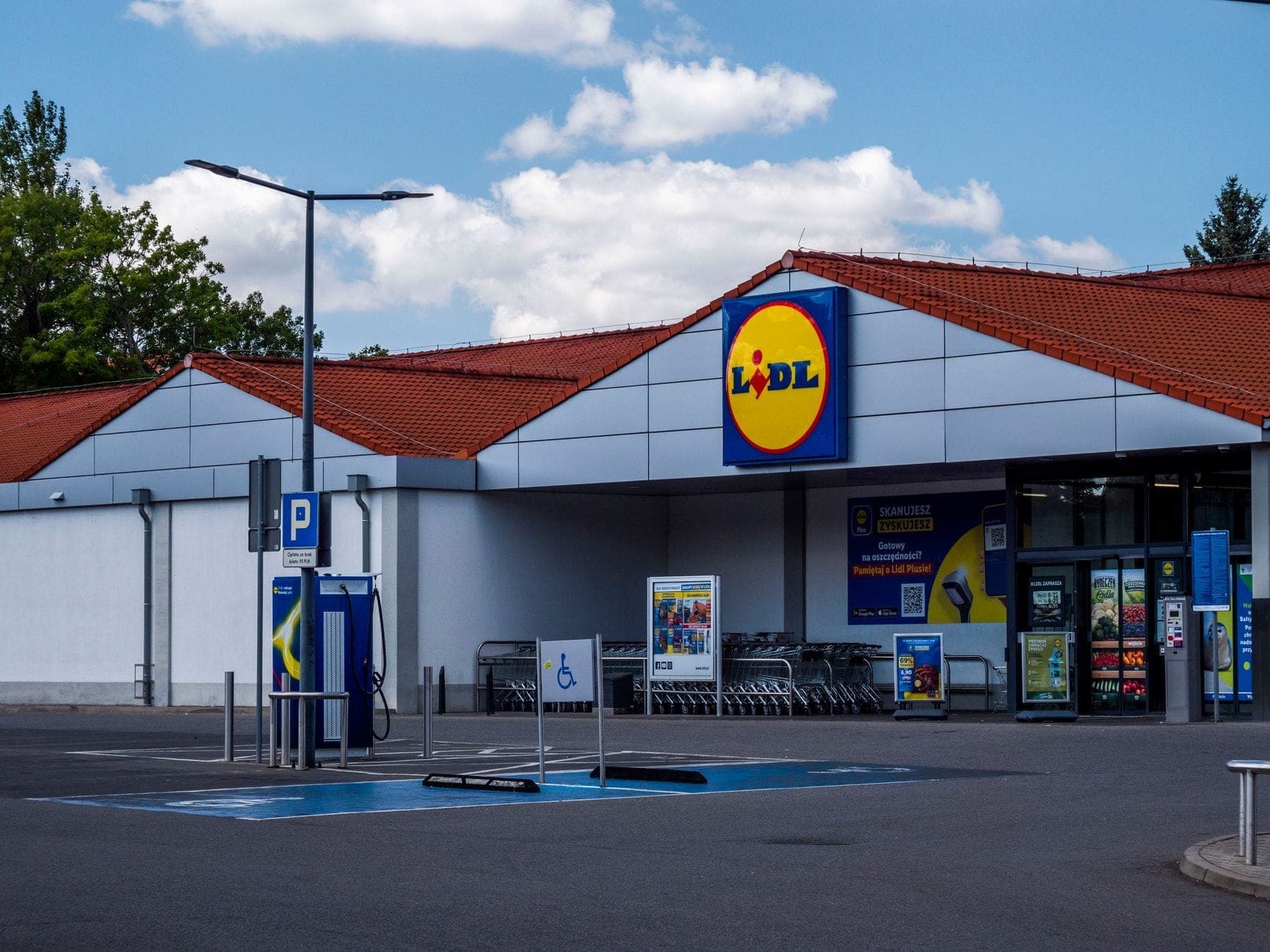 Vista esterna di un supermercato Lidl con posti auto e carrelli della spesa fuori sotto un cielo azzurro.