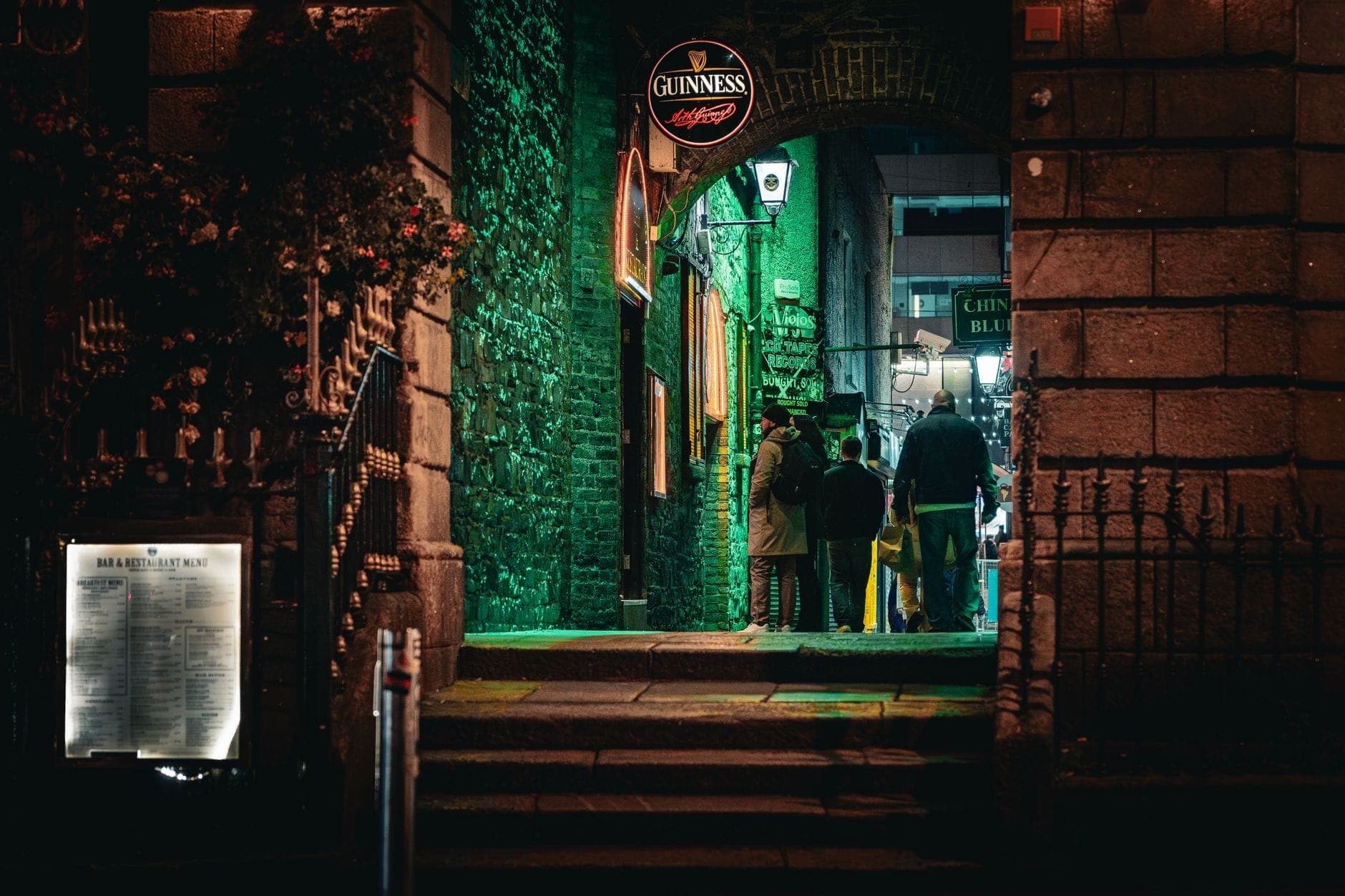 Vista notturna dell'ingresso di un quartiere di pub a Dublino con un'insegna Guinness ben visibile e persone riunite sotto luci verdi