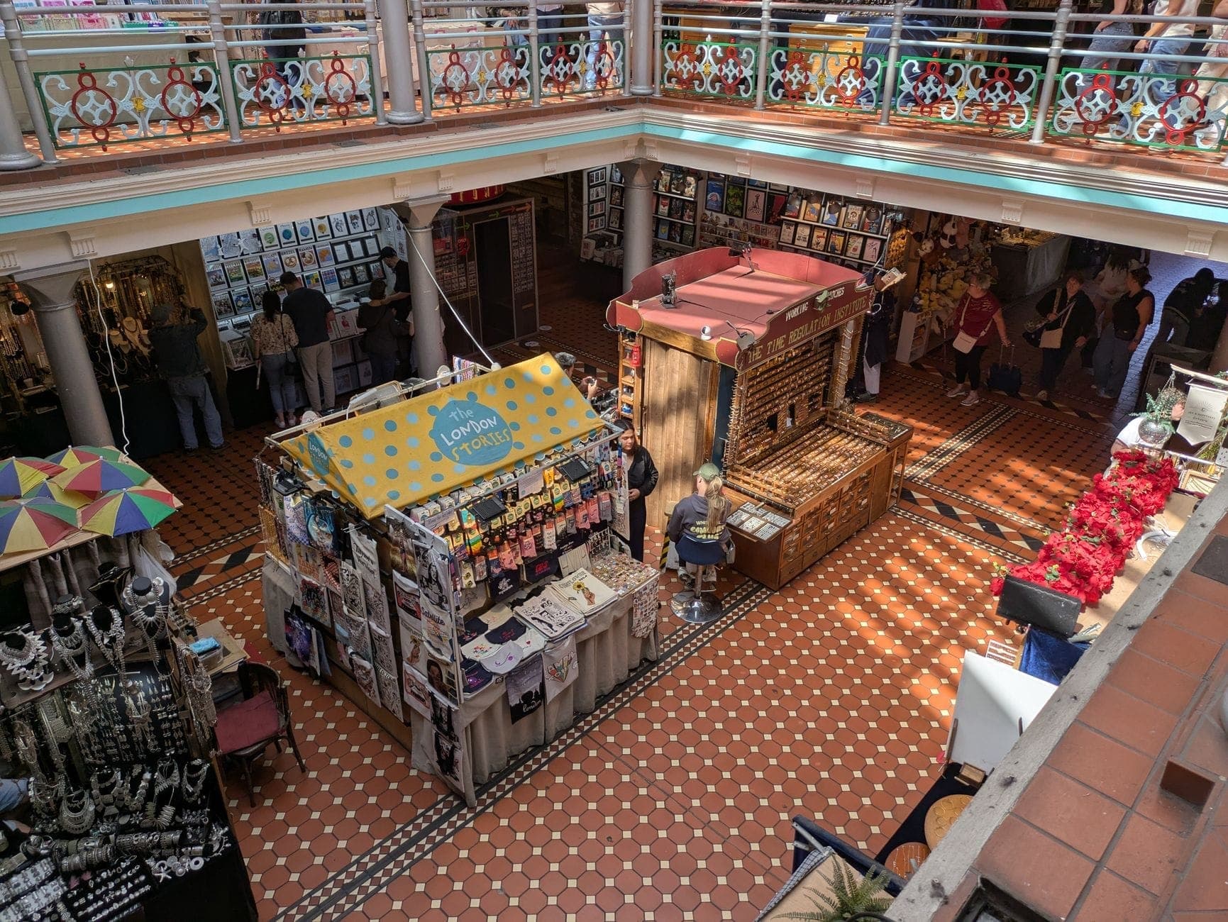 Überdachter Markt im viktorianischen Stil in Dublin mit Fliesenboden, bunten Ständen mit Kunsthandwerk und Schmuck sowie Besuchern auf zwei Ebenen.
