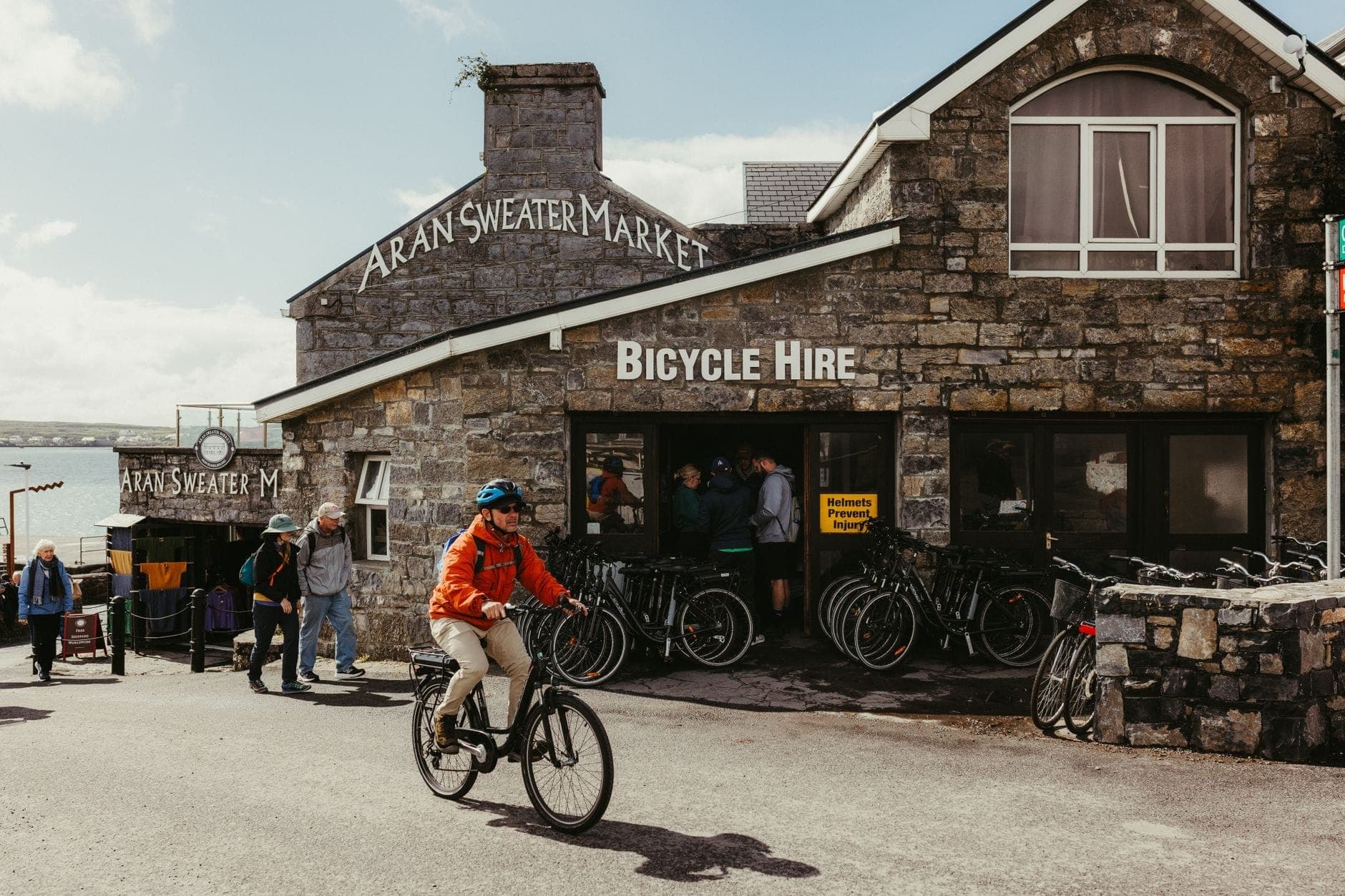 Steingebäude mit dem Schild 'Aran Sweater Market' in Dublin, Menschen, die zu Fuß gehen und Fahrrad fahren, was auf authentische irische Waren hindeutet.