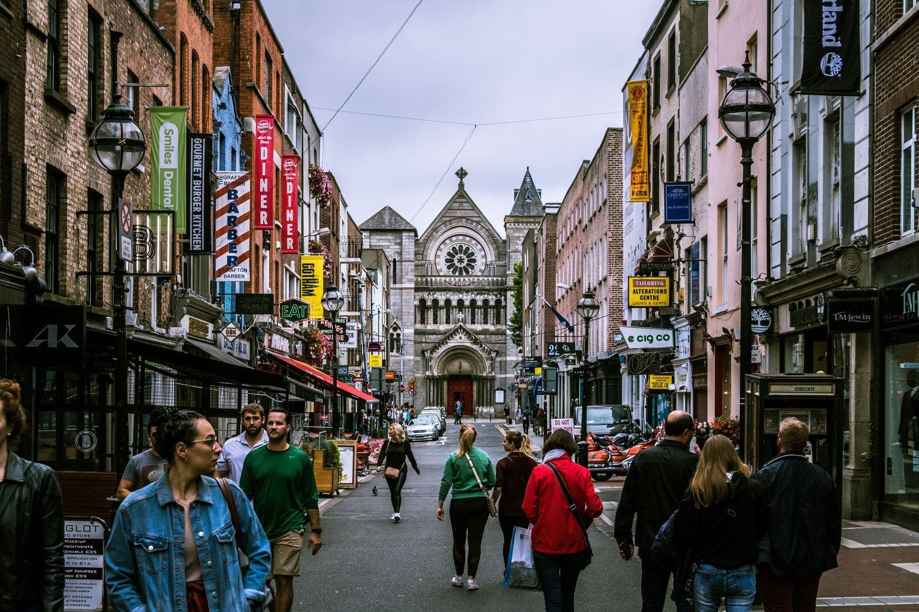Rue animée de Dublin avec des passants devant boutiques et pubs, enseignes colorées et une église historique au fond de la rue.