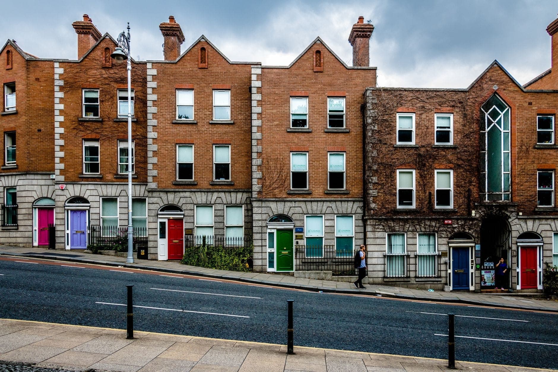 Une rangée de maisons de ville géorgiennes en brique à Dublin, avec des portes d'entrée colorées et des fenêtres en arc le long d'une rue légèrement vallonnée.
