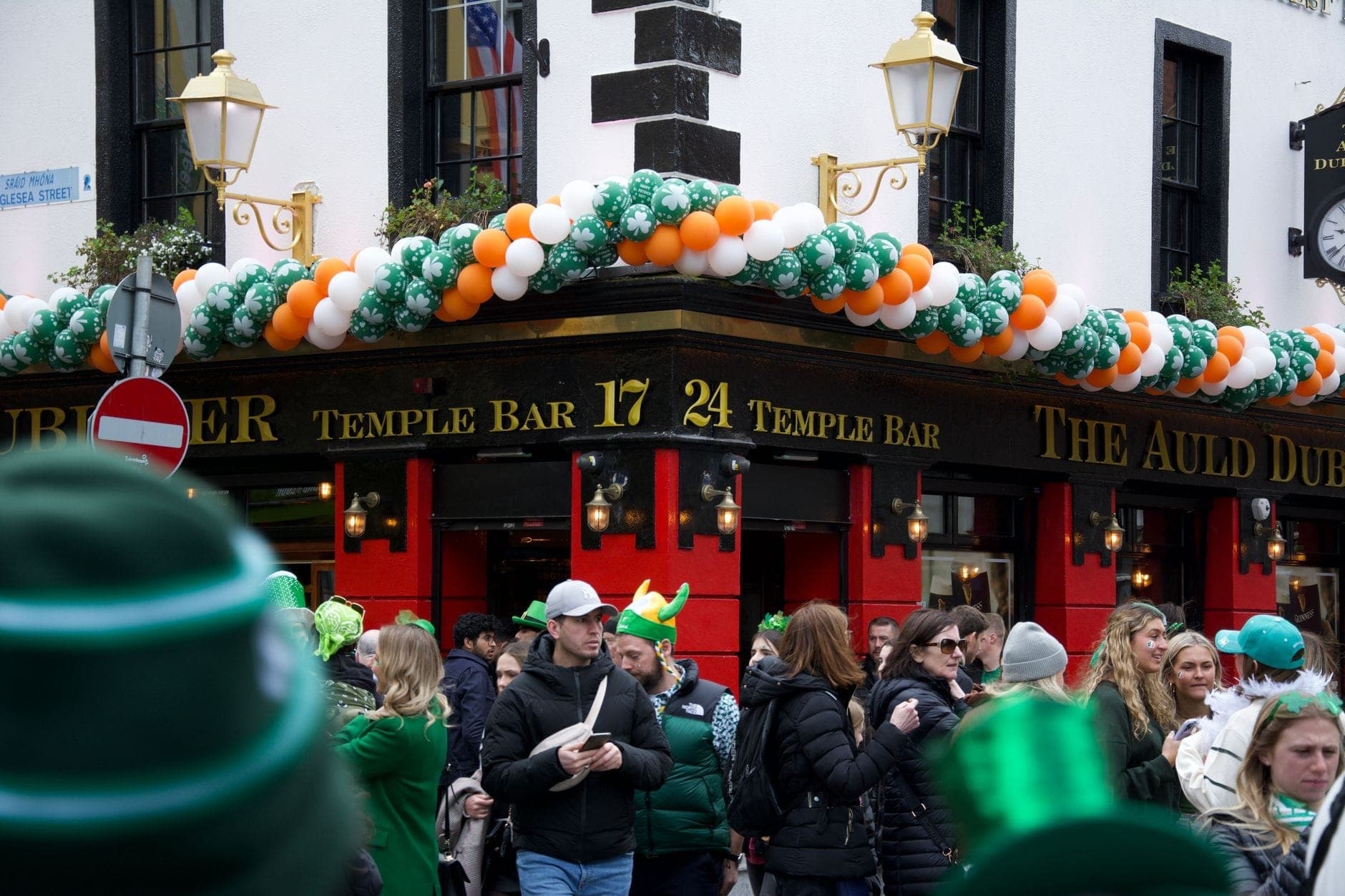 Tłumy w świątecznych strojach przed Temple Bar w Dublinie, udekorowanym zielonymi, białymi i pomarańczowymi balonami z okazji obchodów Dnia Świętego Patryka.