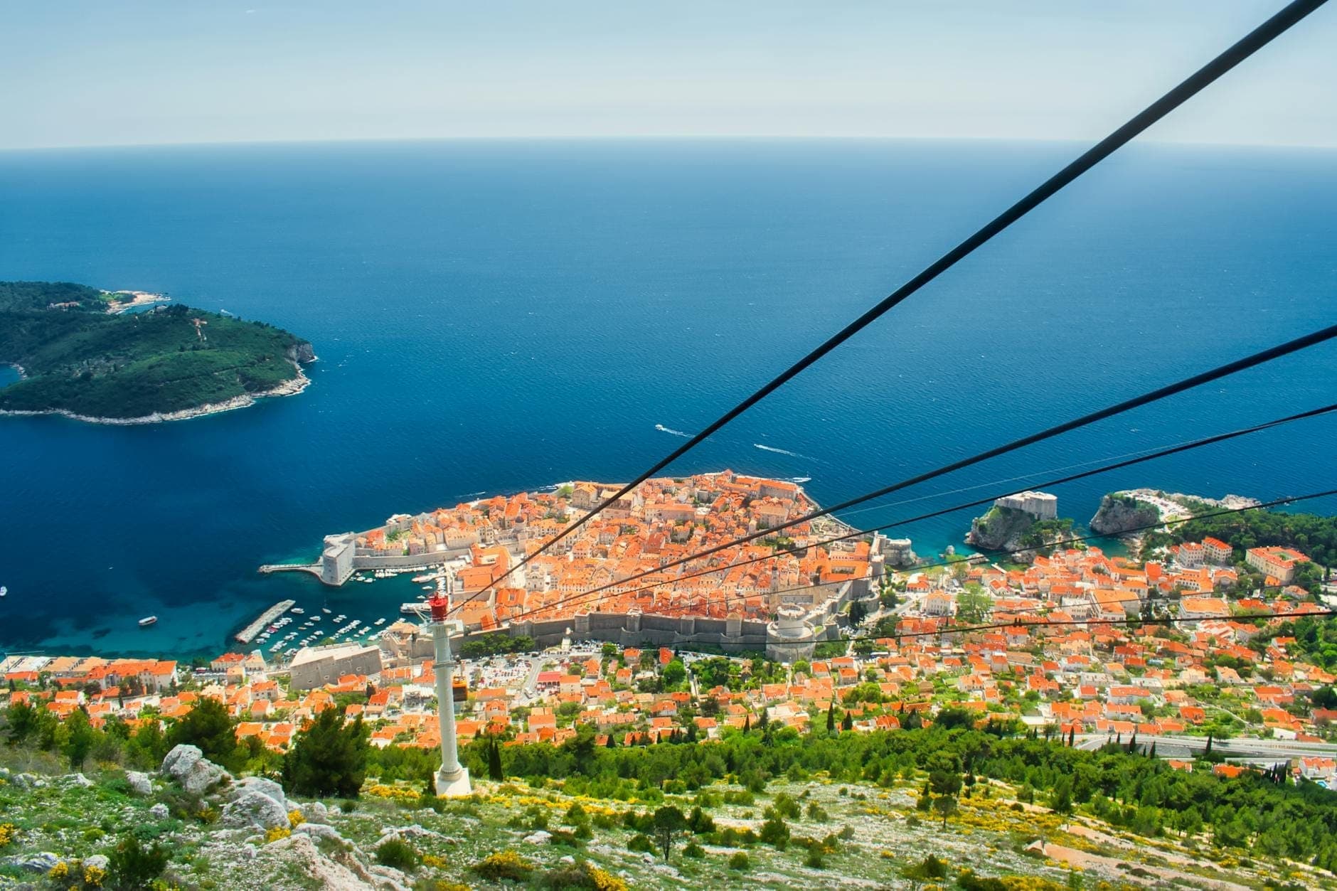 Nhìn từ trên cao theo tuyến cáp treo Dubrovnik, bao quát Phố Cổ, biển Adriatic, hòn đảo lân cận và những mái ngói đất nung dưới bầu trời xanh trong.