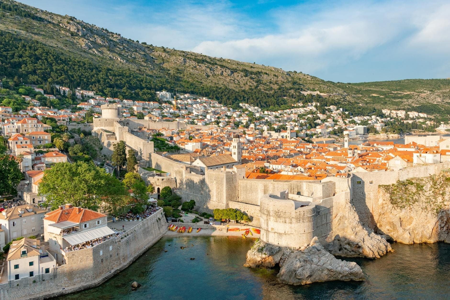 Toàn cảnh tường thành Dubrovnik bao quanh Phố cổ, với mái ngói đỏ, biển xanh trong vắt và đồi xanh dưới nắng.