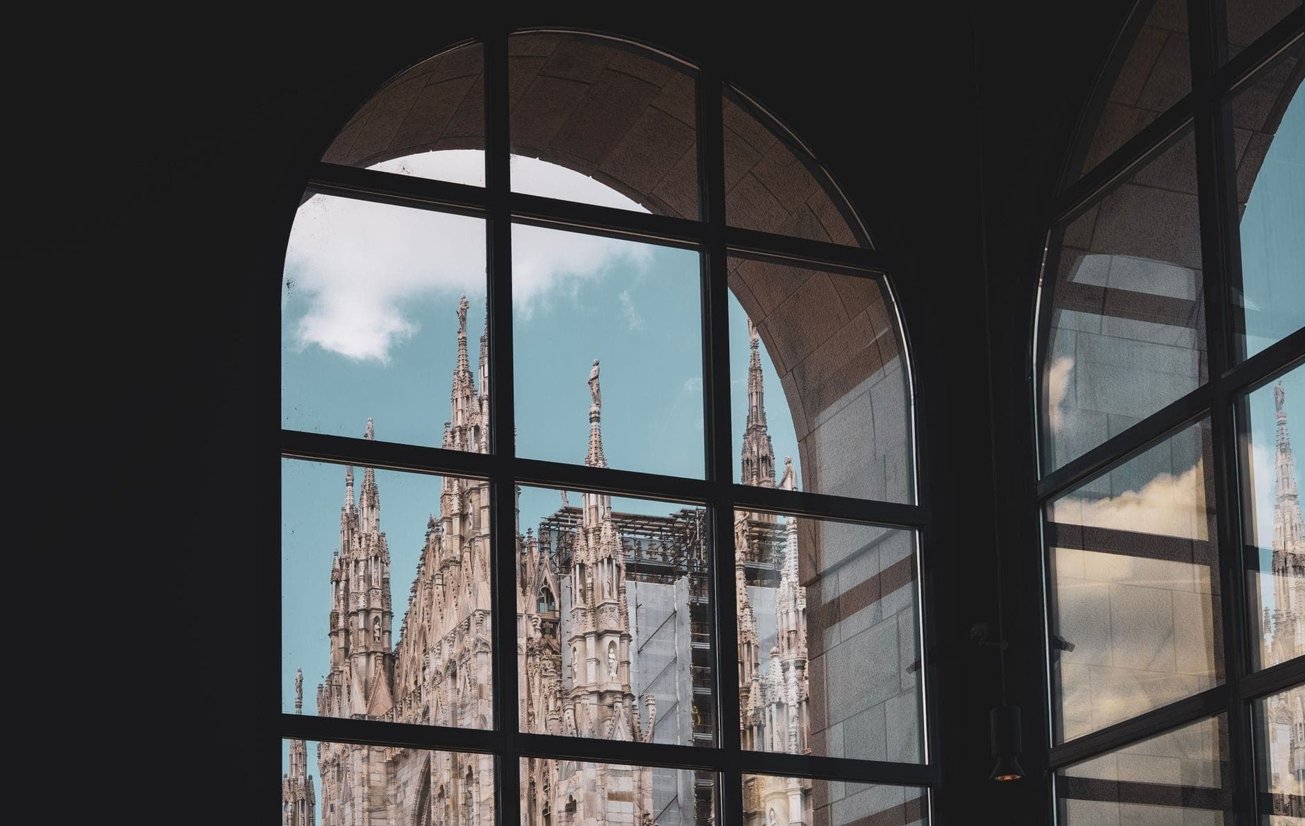 The spires of Milan’s cathedral are seen through grand arched museum windows, blending the Duomo’s ornate Gothic details with the quiet interior setting.