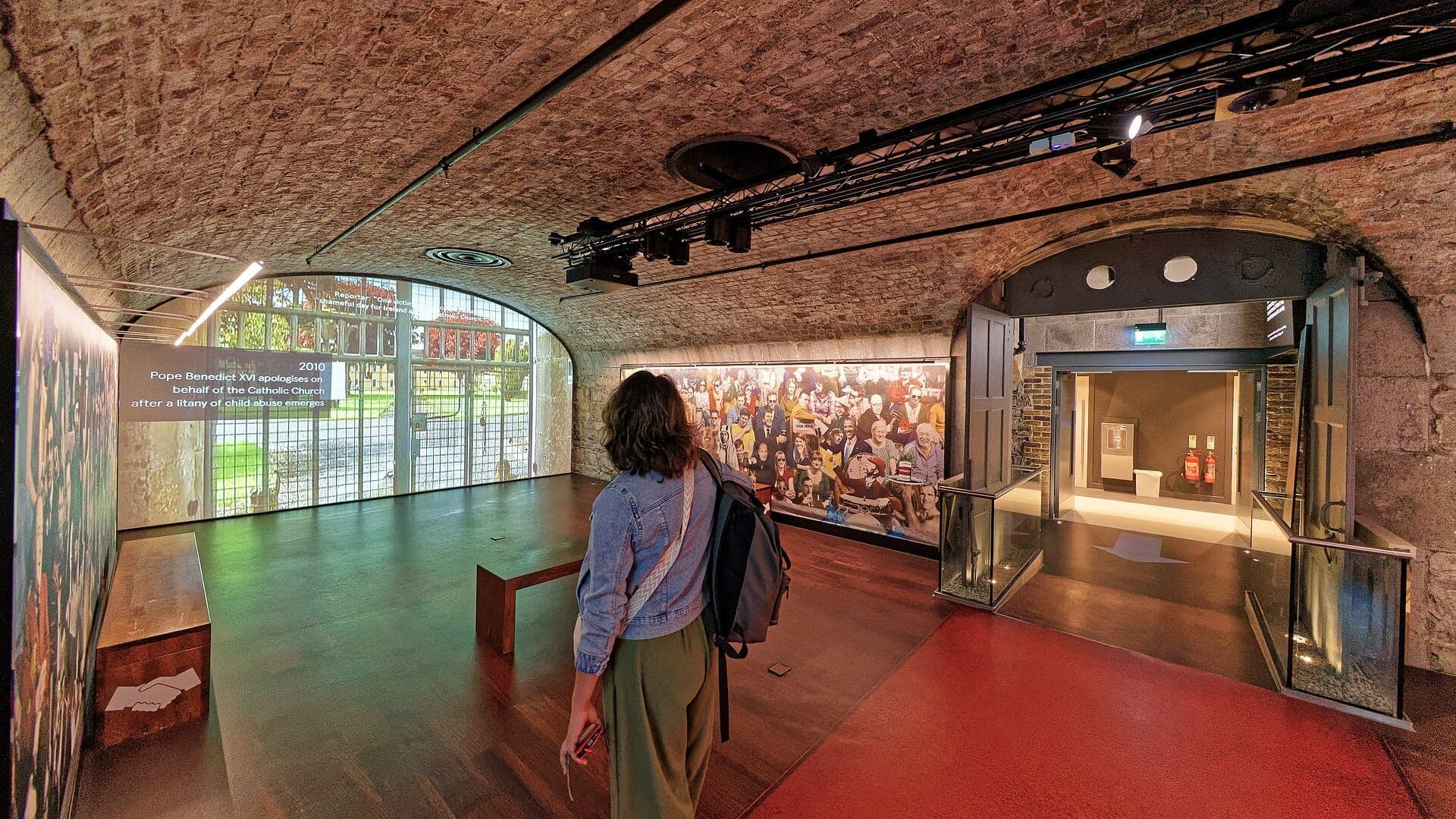 Odwiedzający spacerujący przez sklepione, kamienne wnętrze EPIC The Irish Emigration Museum, z widocznymi eksponatami i historycznymi projekcjami.