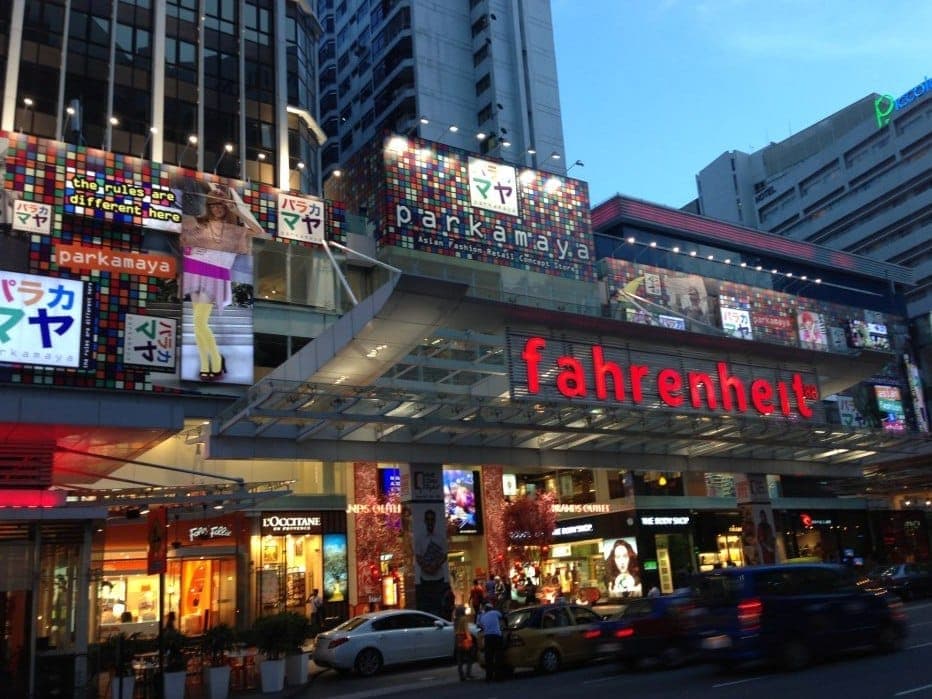 Cảnh bên ngoài trung tâm mua sắm Fahrenheit 88 tại Bukit Bintang, với các biển hiệu sáng rực, quảng cáo đầy màu sắc và giao thông đông đúc trên phố vào buổi tối.