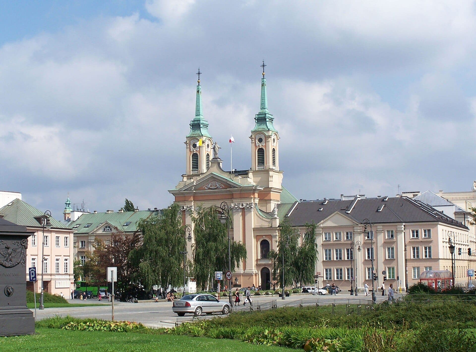 Die Feldkathedrale der Polnischen Armee in Warschau weist Zwillingstürme, eine helle Fassade und grüne Dächer auf, umgeben von Bäumen und historischen Gebäuden.