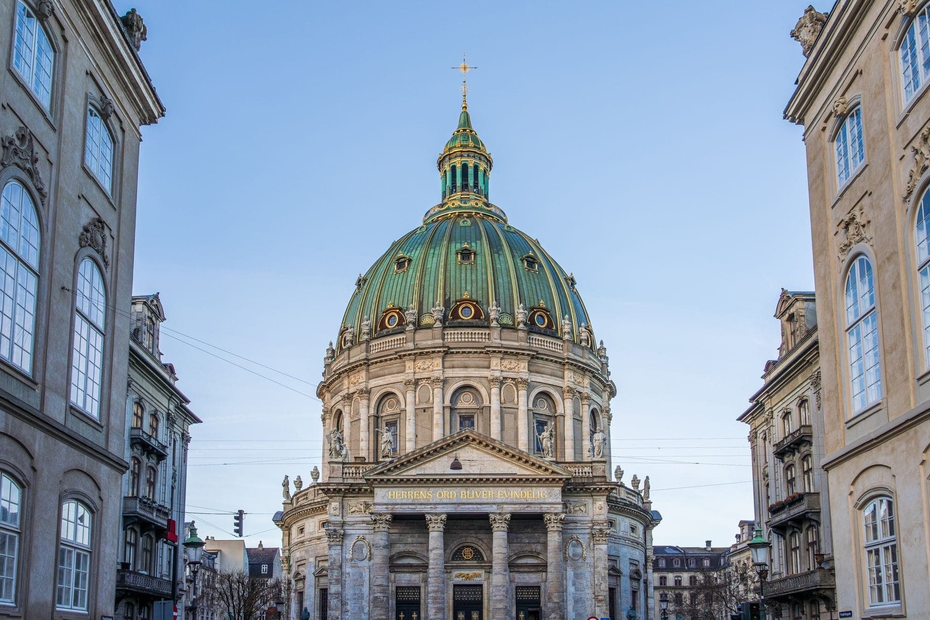 Die Frederikskirche in Kopenhagen mit ihrer imposanten grünen Kupferkuppel über dem Eingang, flankiert von eleganten Gebäuden bei klarem Himmel.
