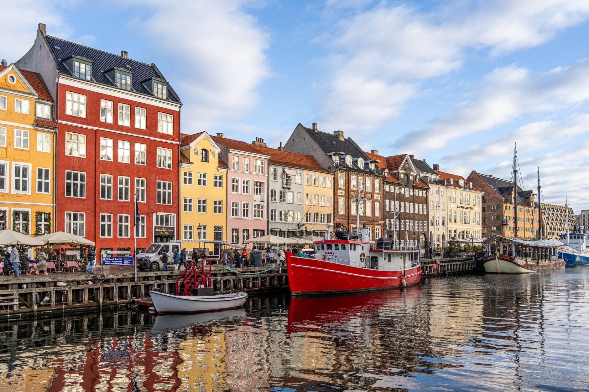 Ang iconic na baybay-dagat ng Nyhavn sa Copenhagen na may makulay na makasaysayang mga gusali, mga nakaponding bangka, at mga taong naglalakad sa masayang pantalan.
