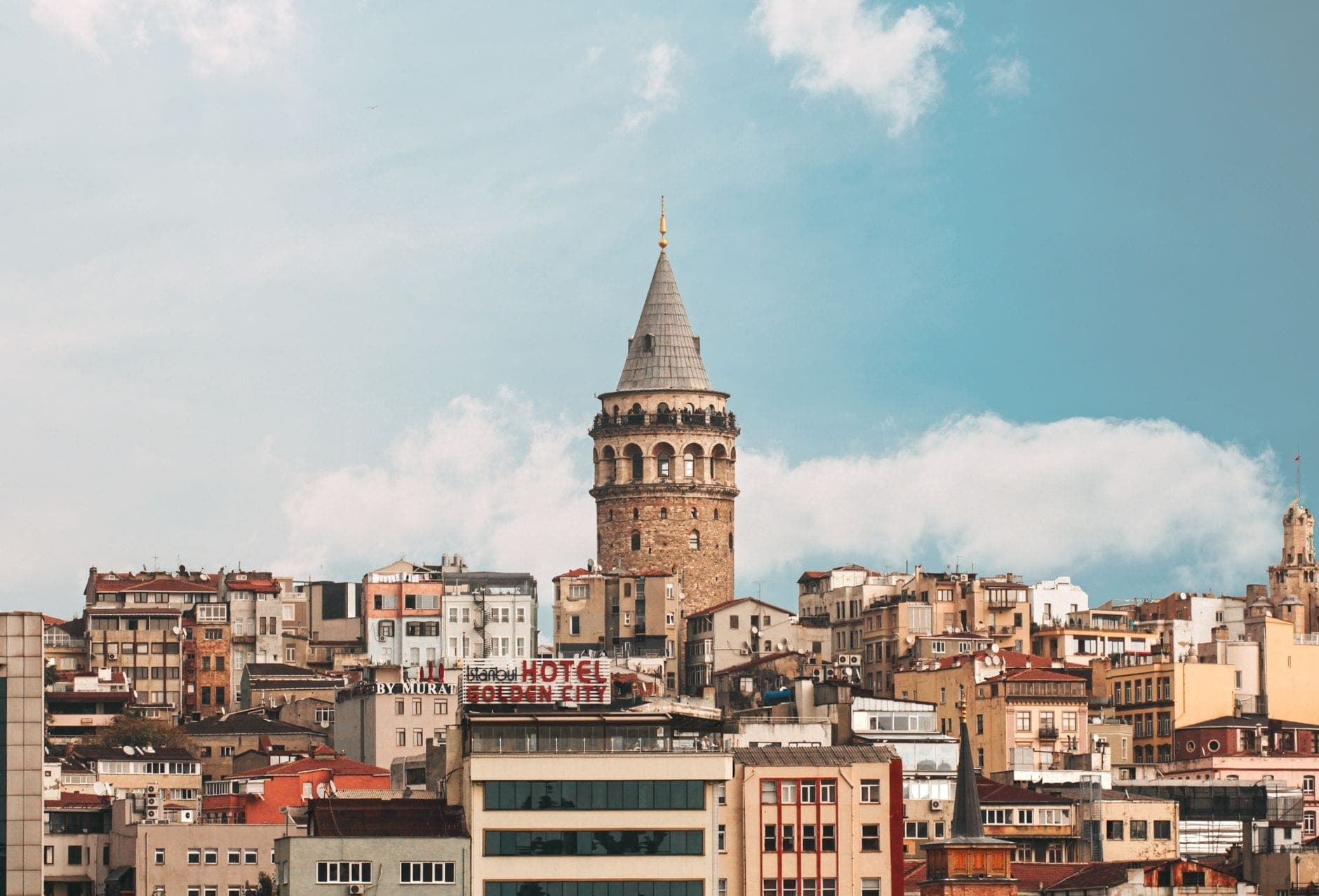 Der Galata-Turm ragt markant über die bunten Stadtgebäude hinaus, vor einem strahlend blauen Himmel mit vereinzelten Wolken in Istanbul, Türkei.