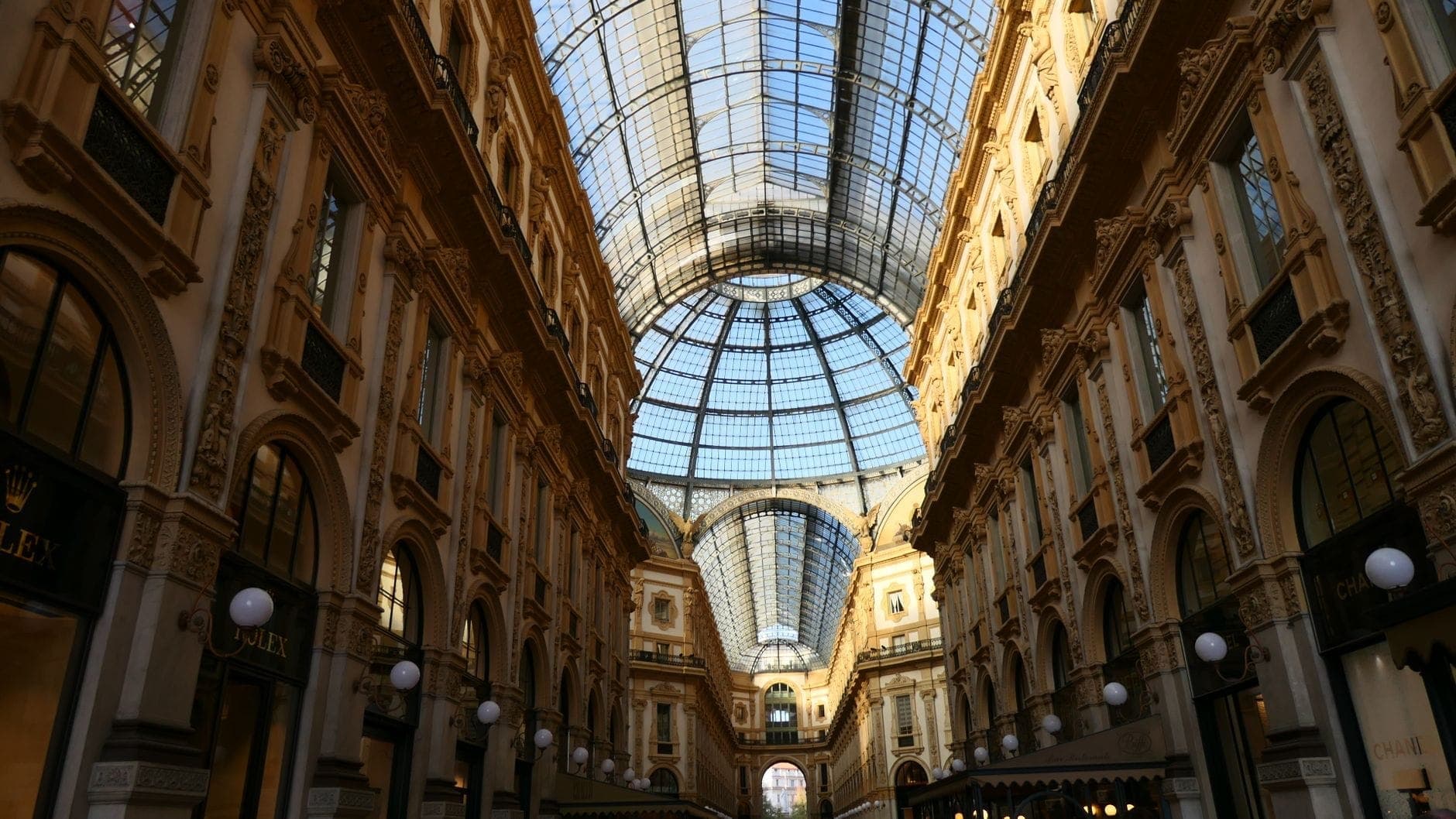 Wide view of the Galleria Vittorio Emanuele II’s ornate glass dome and elegant 19th-century architecture, with sunlight illuminating the spacious arcade and luxury shopfronts in Milan.